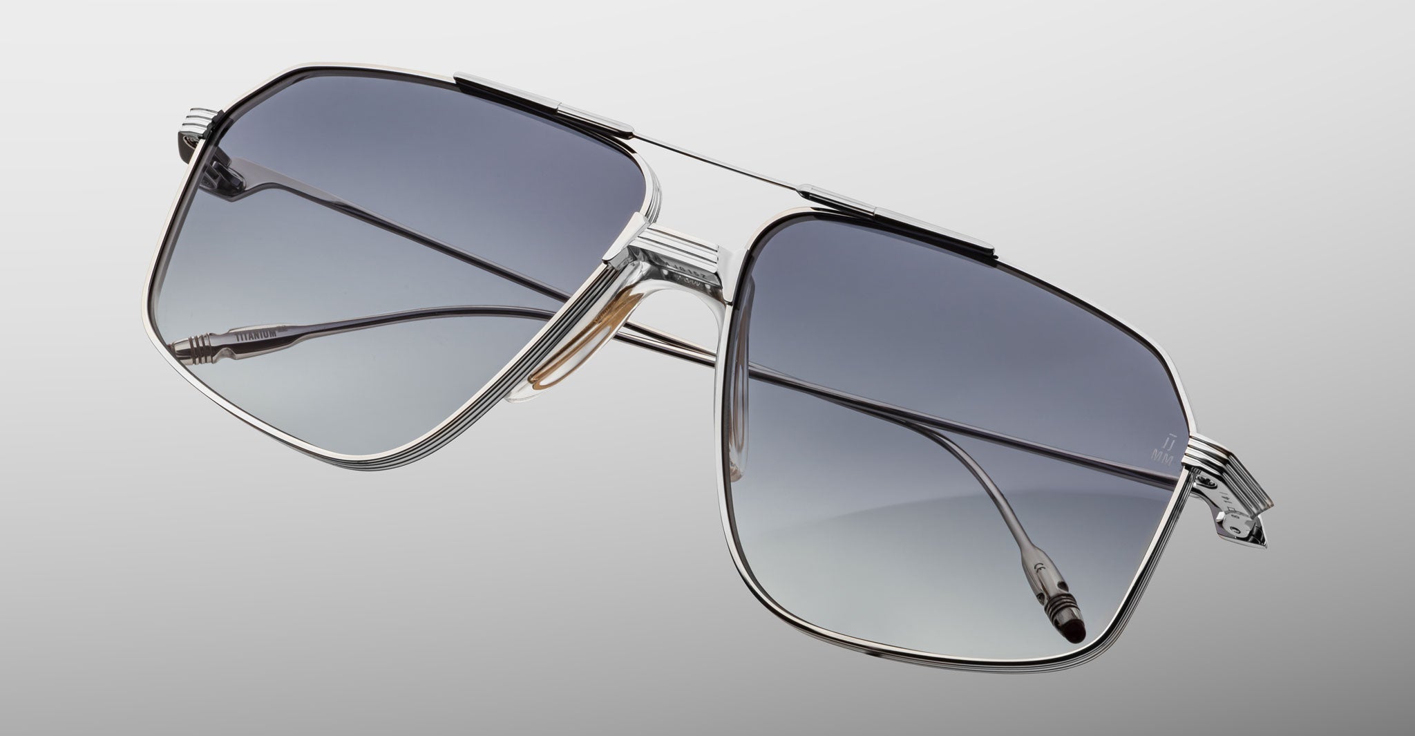 The Jacques Marie Mage Jagger sunglasses by Jacques Marie Mage feature silver oversized aviator frames in beta titanium with gradient gray lenses, inspired by the iconic Jagger style, displayed on a light gray background.
