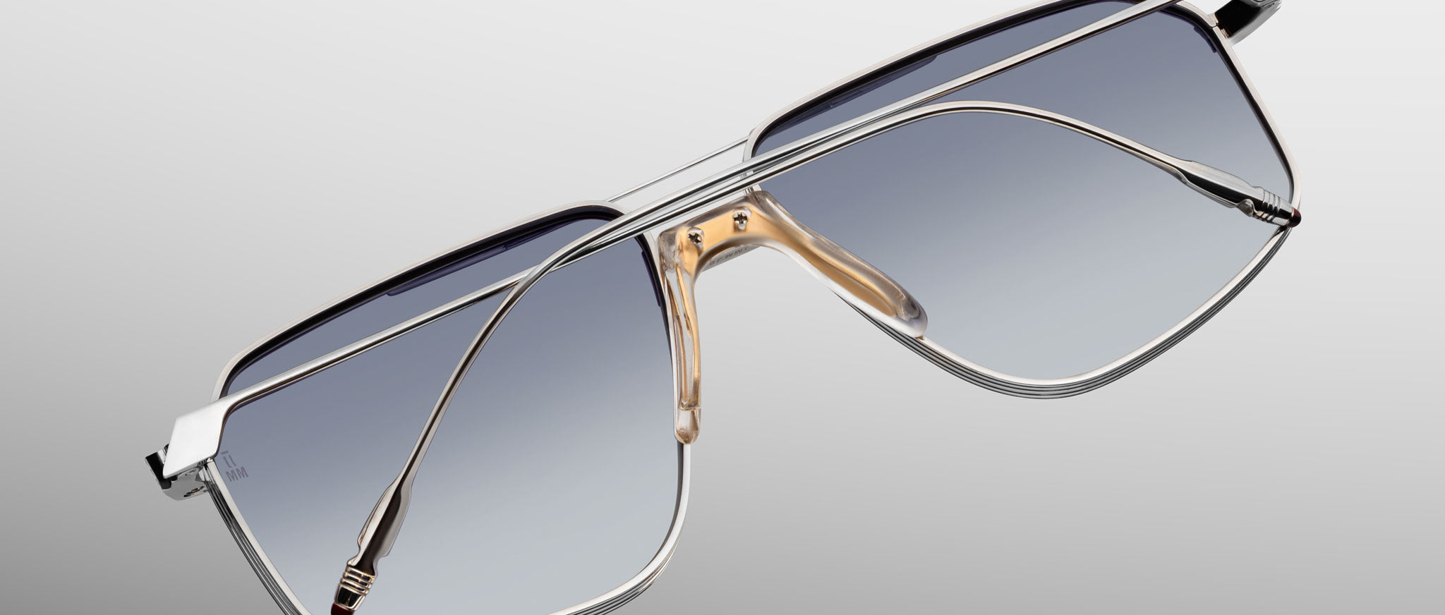 Jacques Marie Mage Jagger: Oversized aviator sunglasses in silver beta titanium with gradient blue lenses and gold nose pads by Jacques Marie Mage, shown on a light gray background for a bold, timeless style.