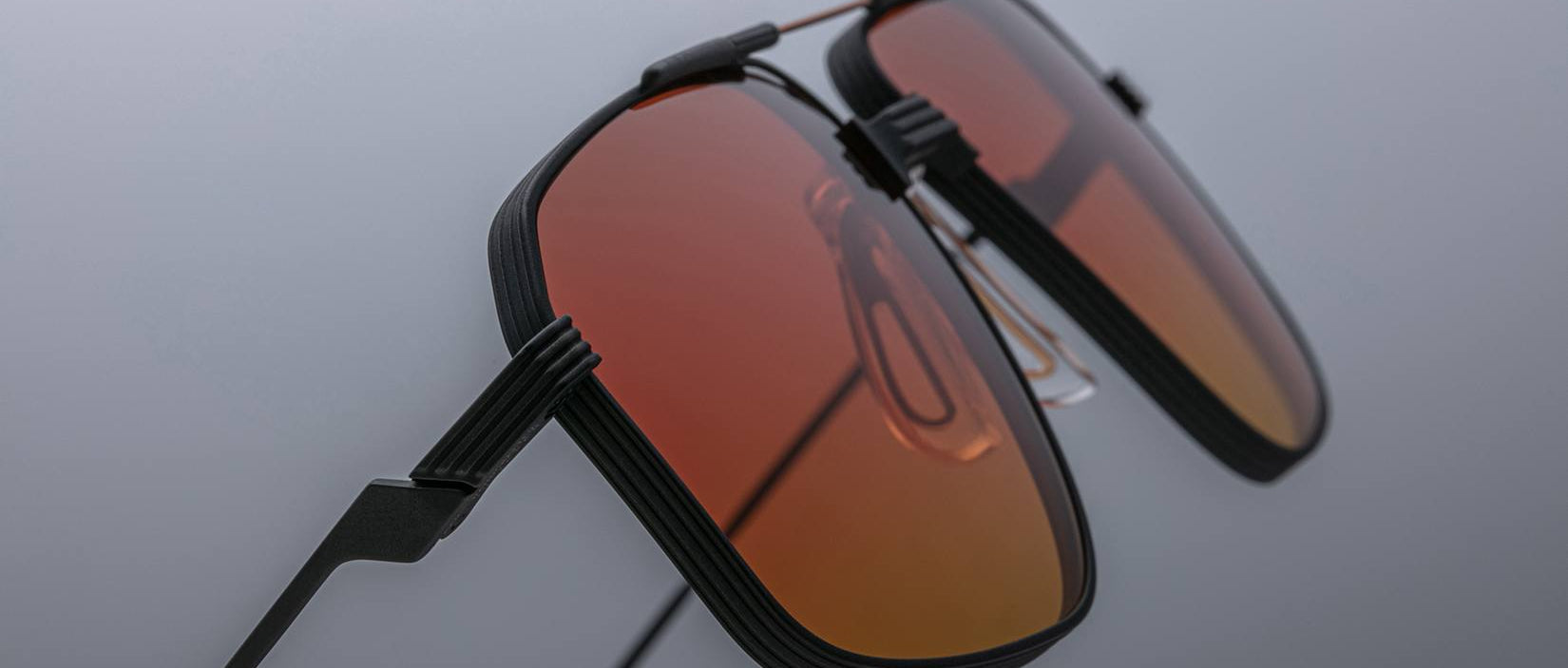 Close-up of Jacques Marie Mage Jagger sunglasses featuring rectangular orange-tinted lenses and black beta titanium frames, set against a neutral background.