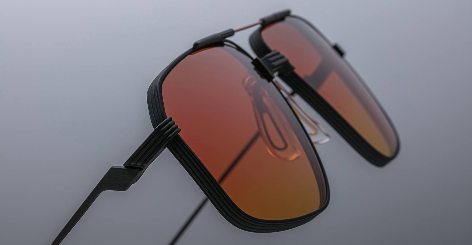 Close-up of Jacques Marie Mage Jagger sunglasses featuring rectangular orange-tinted lenses and black beta titanium frames, set against a neutral background.