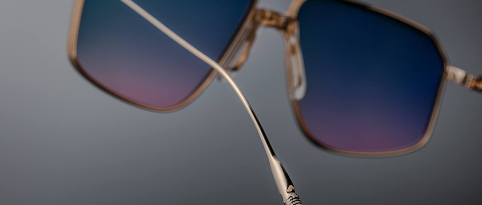 Close-up of Jacques Marie Mage Jagger oversized aviator sunglasses by Jacques Marie Mage, featuring gold-rimmed frames, blue gradient lenses, and a focus on the temple arm's beta titanium build with detailed tip design.