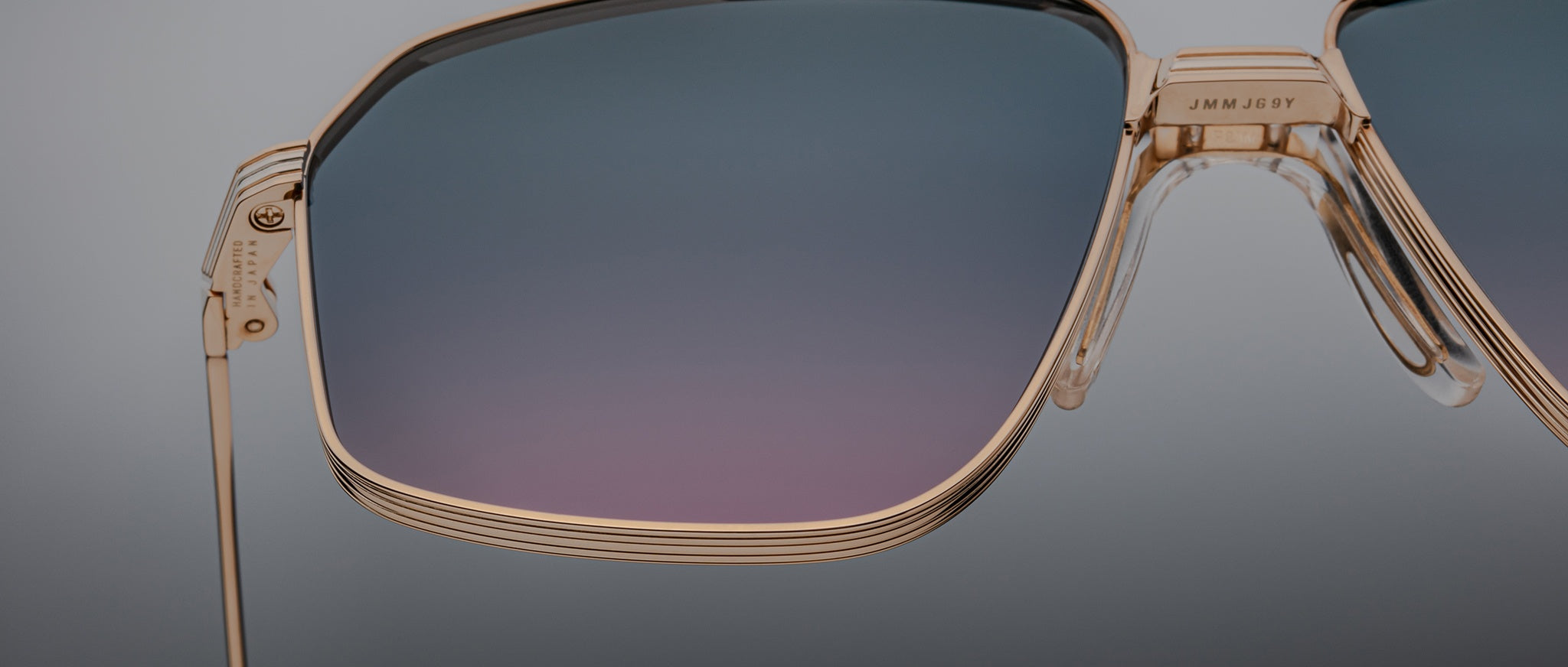 Close-up of Jacques Marie Mage Jagger sunglasses by Jacques Marie Mage, featuring oversized aviator gold frames and gradient blue-purple lenses, set against a plain background.