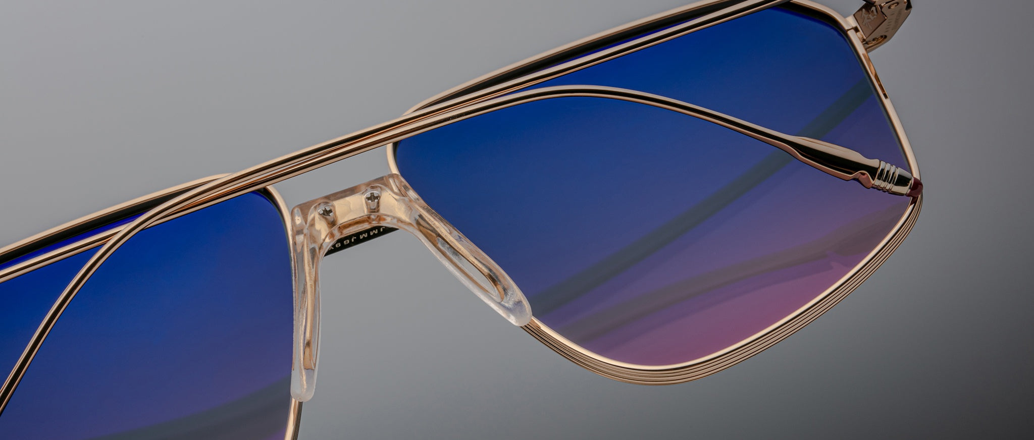 Close-up of Jacques Marie Mage Jagger oversized aviator sunglasses by Jacques Marie Mage, featuring gold metal frames and blue-to-purple gradient lenses, set against a neutral background.