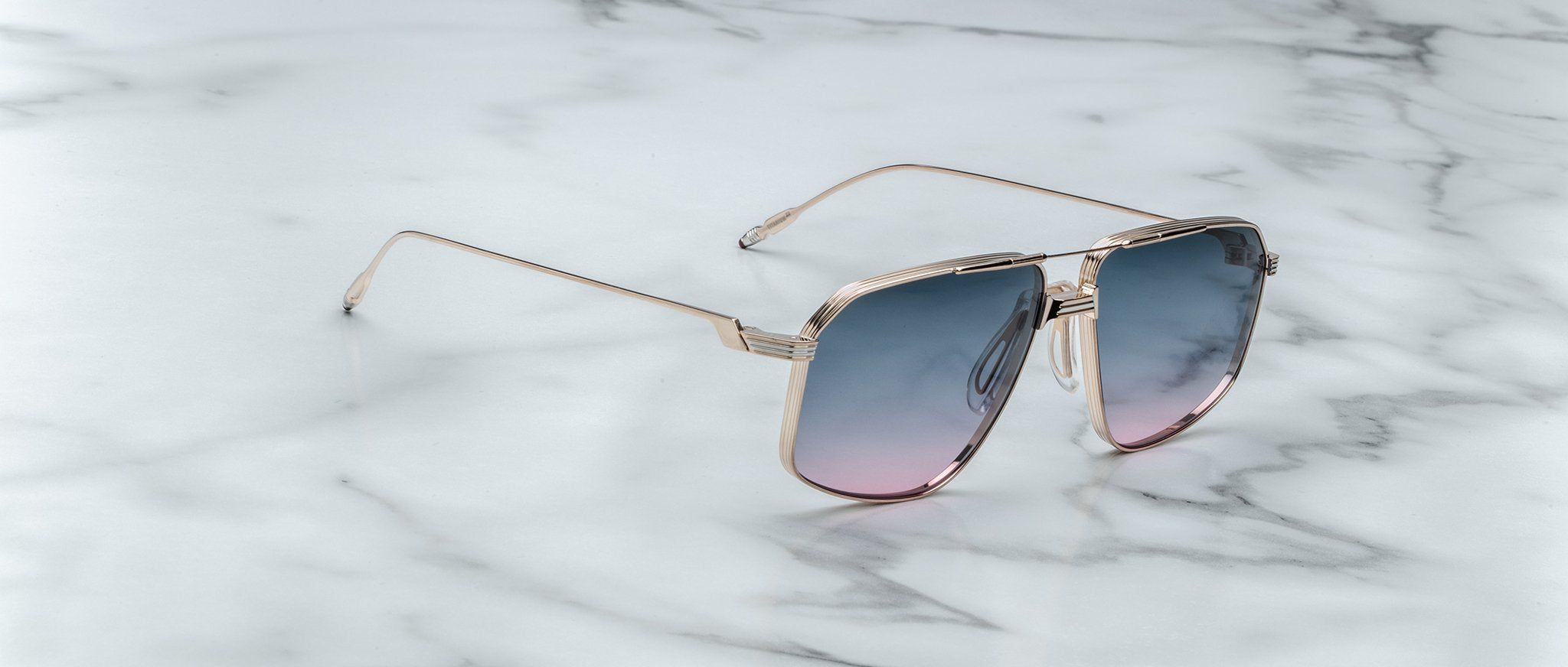 Jacques Marie Mage Jagger gold-framed oversized aviator sunglasses with gradient blue-pink lenses by Jacques Marie Mage, elegantly displayed on a white marble surface.
