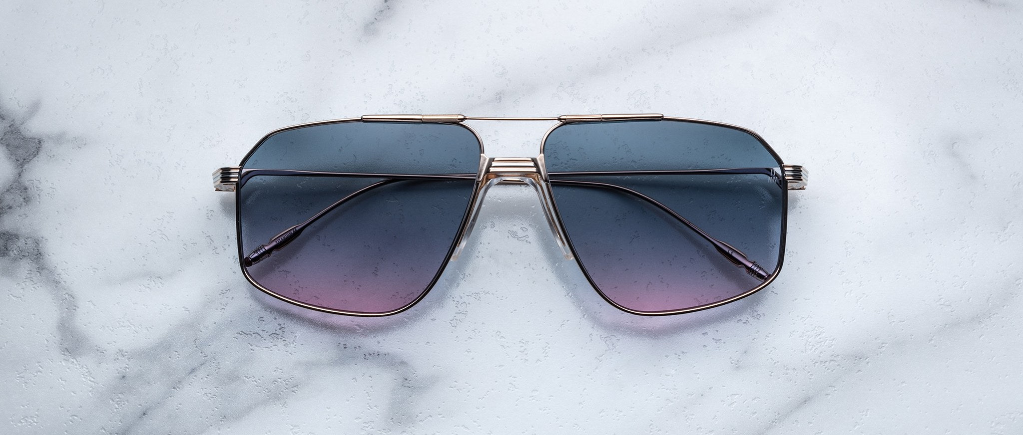 The Jacques Marie Mage Jagger oversized aviator sunglasses, featuring gradient blue lenses and sleek metal frames, rest elegantly on a white marble surface.