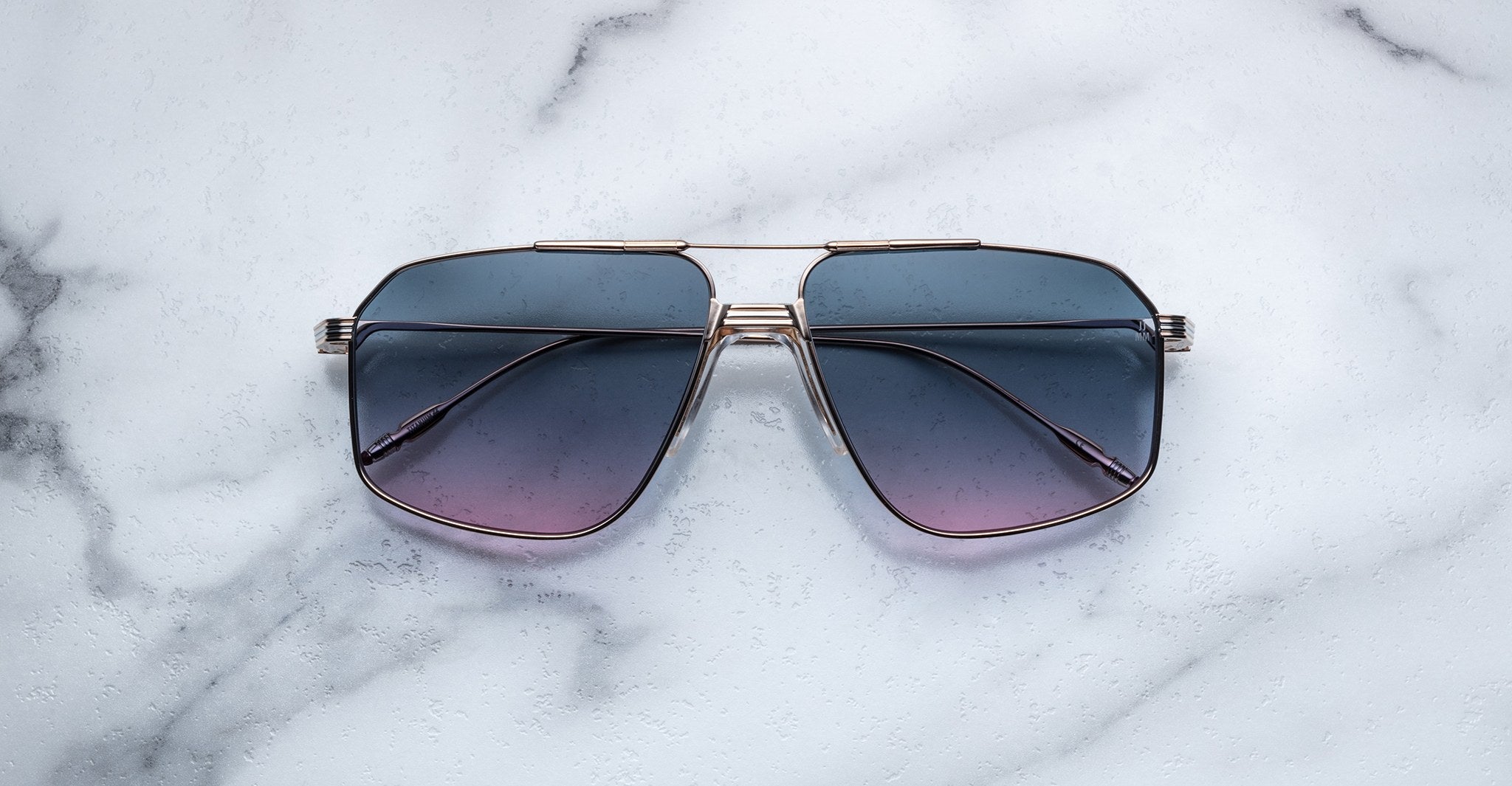 The Jacques Marie Mage Jagger oversized aviator sunglasses, featuring gradient blue lenses and sleek metal frames, rest elegantly on a white marble surface.