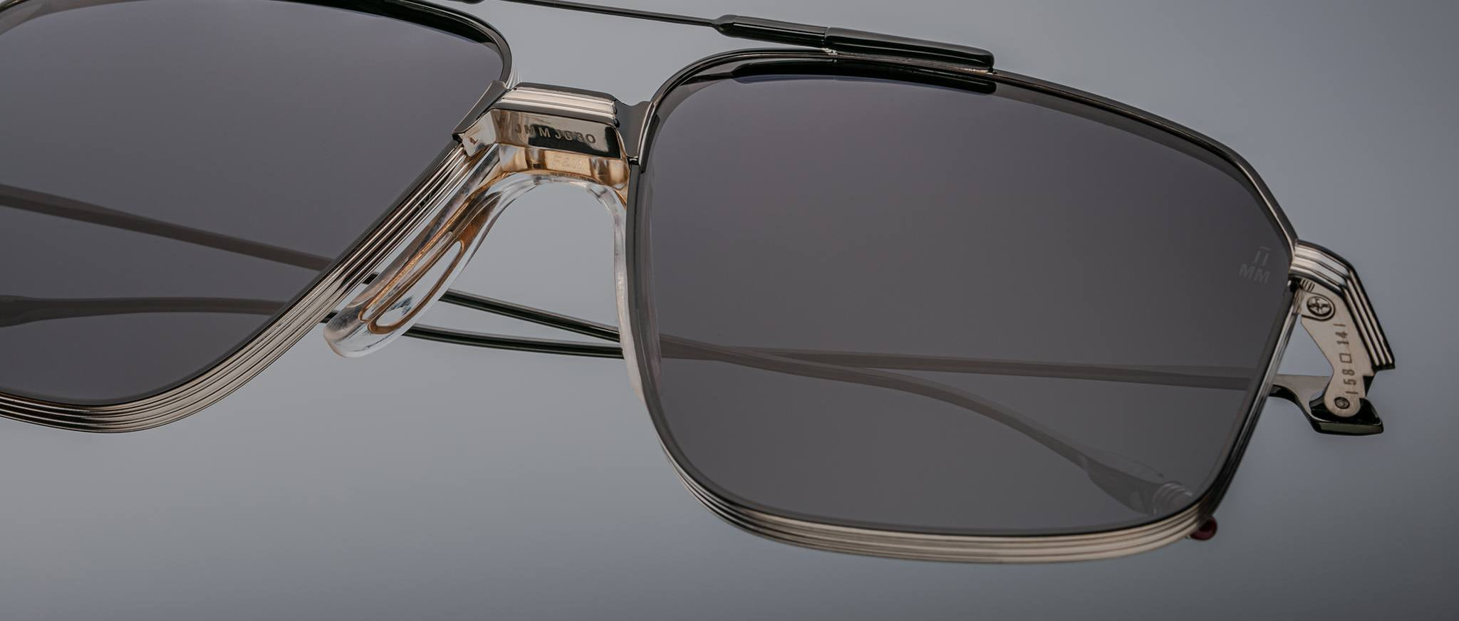 Close-up of Jacques Marie Mage Jagger rectangular sunglasses by Jacques Marie Mage, featuring dark lenses and metallic beta titanium frames against a plain background.