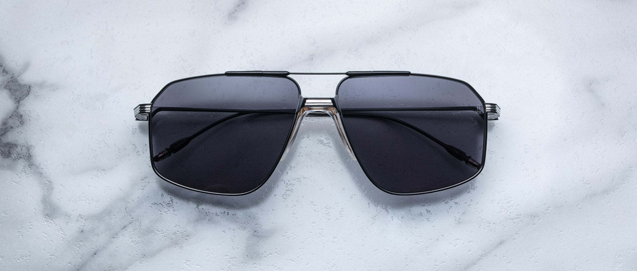 Jacques Marie Mage Jagger oversized aviator sunglasses by Jacques Marie Mage, featuring dark lenses and a silver beta titanium frame, are displayed on a white marble surface.