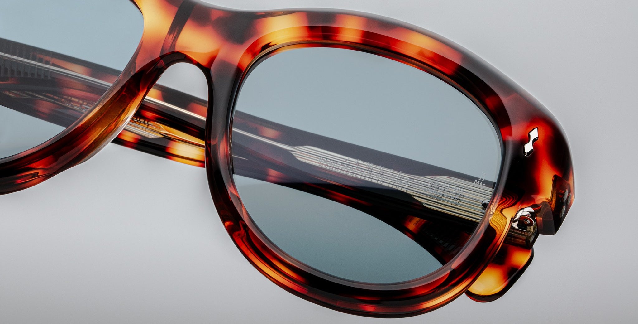 Close-up of Jacques Marie Mage Jennie sunglasses, tortoiseshell frame, blue lenses, silver accent at the hinge.