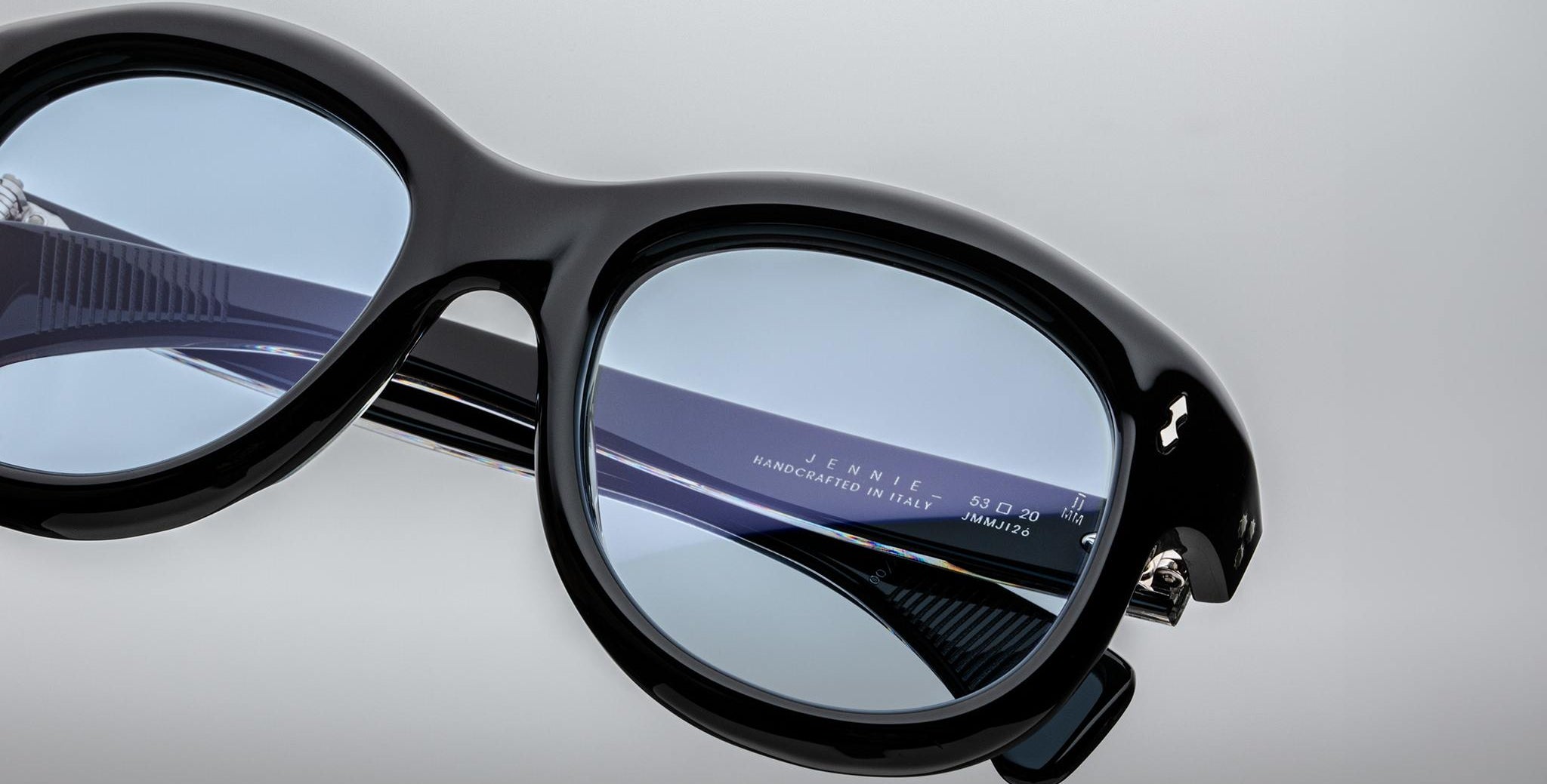 Close-up of Jacques Marie Mage Jennie sunglasses in black with blue-tinted lenses, UV protection details visible inside the temple.