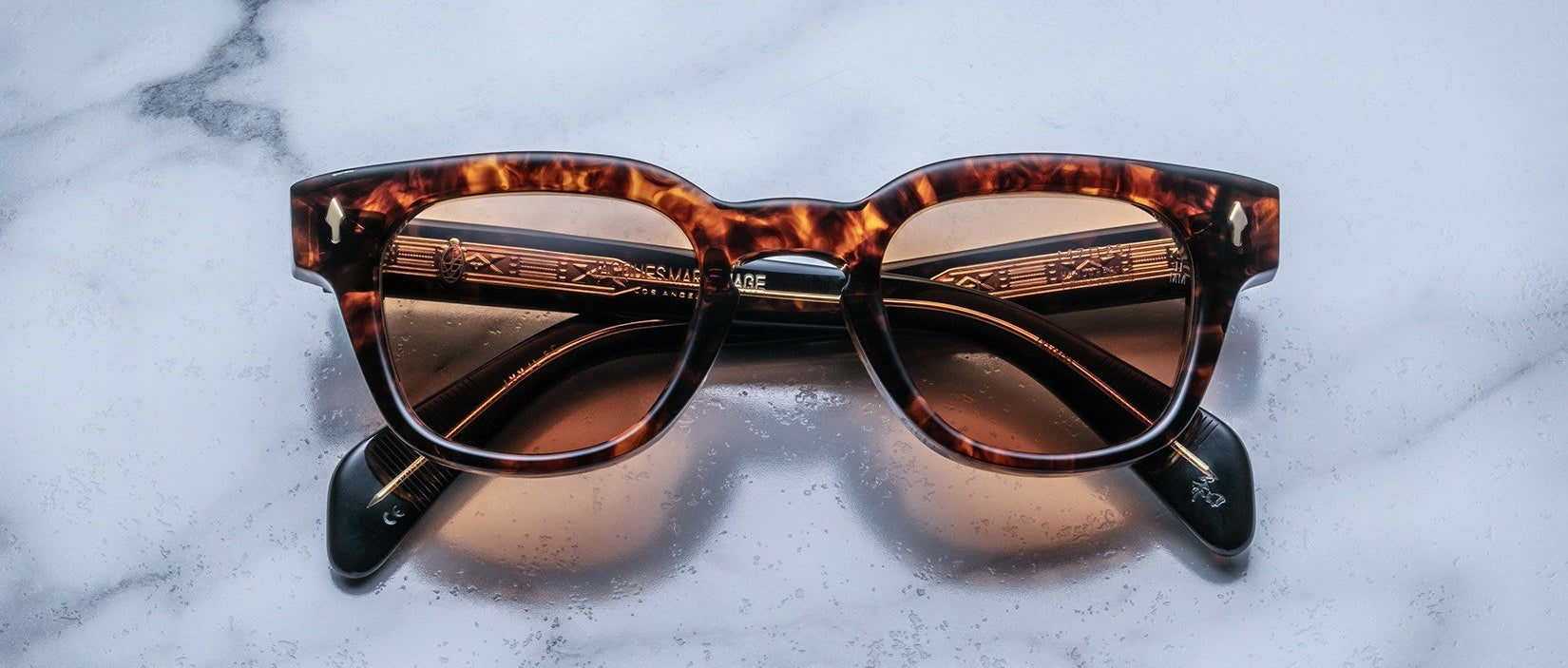 Jacques Marie Mage Julien in Argyle rectangular sunglass in warm tortoiseshell acetate with amber and dark brown marbling, featuring a keyhole bridge, signature arrowhead front pins, and exposed metal core detailing within the temples, shown with lightly tinted lenses.