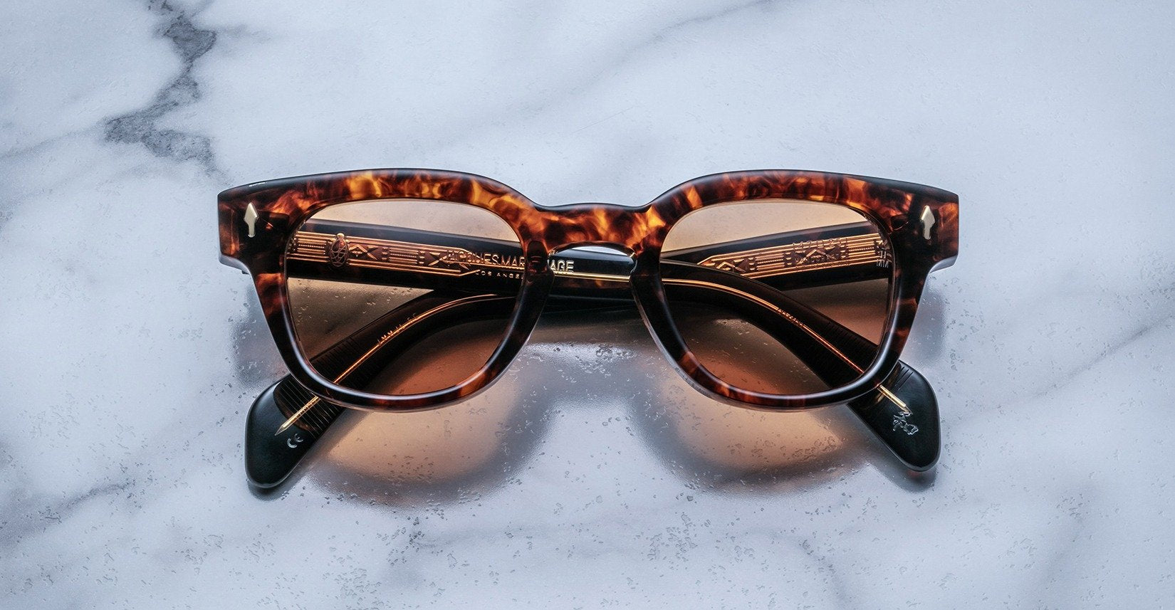 Jacques Marie Mage Julien in Argyle rectangular sunglass in warm tortoiseshell acetate with amber and dark brown marbling, featuring a keyhole bridge, signature arrowhead front pins, and exposed metal core detailing within the temples, shown with lightly tinted lenses.