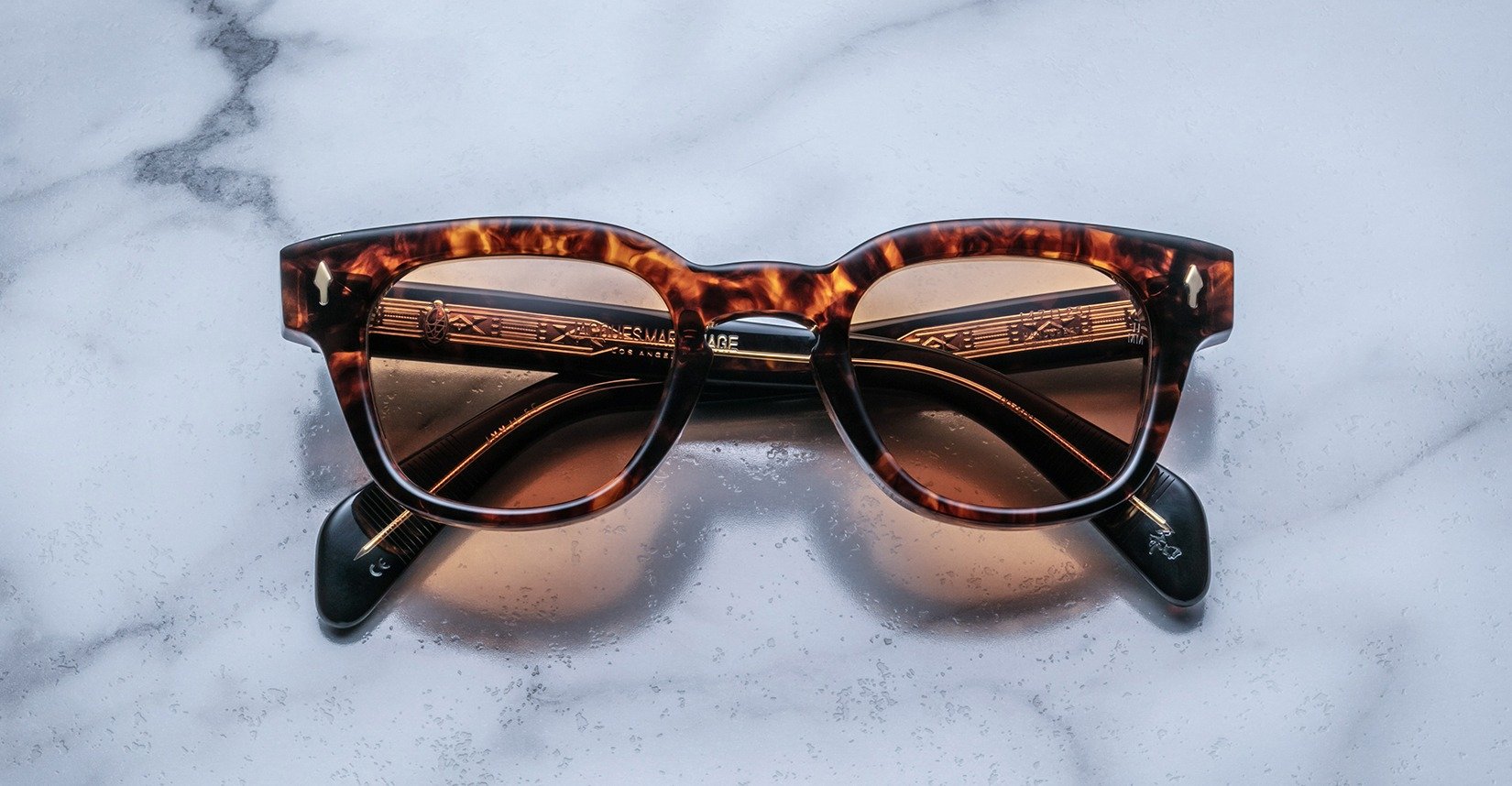 Jacques Marie Mage Julien in Argyle rectangular sunglass in warm tortoiseshell acetate with amber and dark brown marbling, featuring a keyhole bridge, signature arrowhead front pins, and exposed metal core detailing within the temples, shown with lightly tinted lenses.