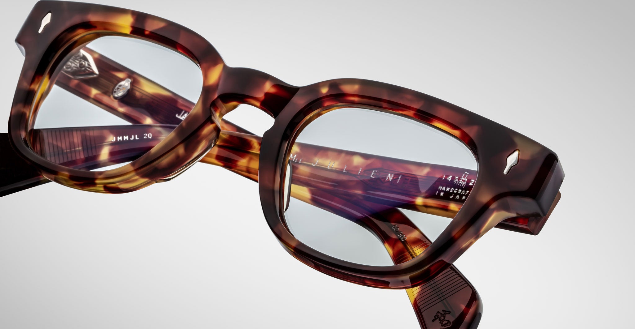 Close-up of Jacques Marie Mage Julien eyeglasses in a tortoiseshell pattern with clear lenses, displaying engraved text and logos on the inside of the temples, set against a plain white background.