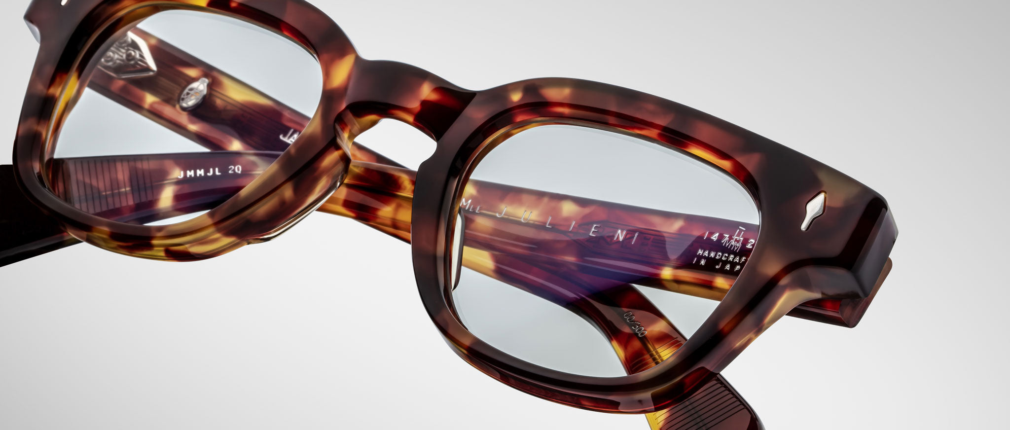 Close-up of Jacques Marie Mage Julien eyeglasses in a tortoiseshell pattern with clear lenses, displaying engraved text and logos on the inside of the temples, set against a plain white background.