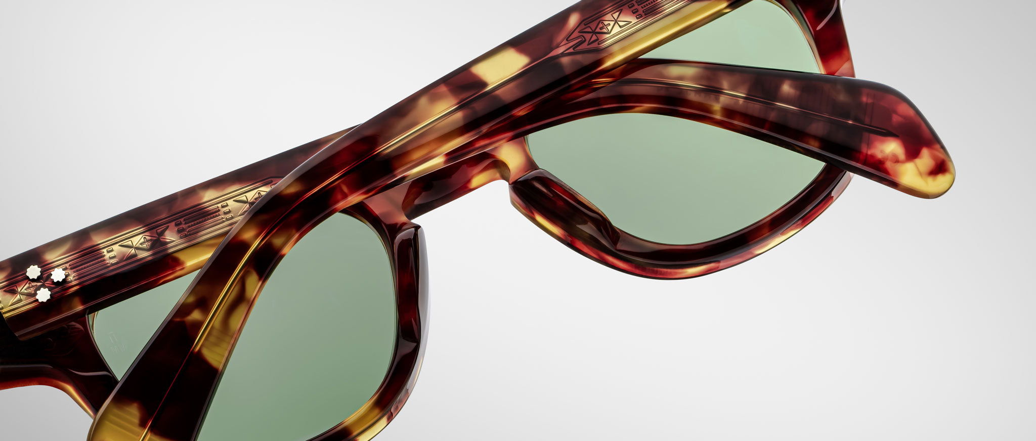 Close-up image of Jacques Marie Mage Julien tortoiseshell sunglasses with green-tinted lenses on a white background. Patterned arms and frame details are clearly visible.