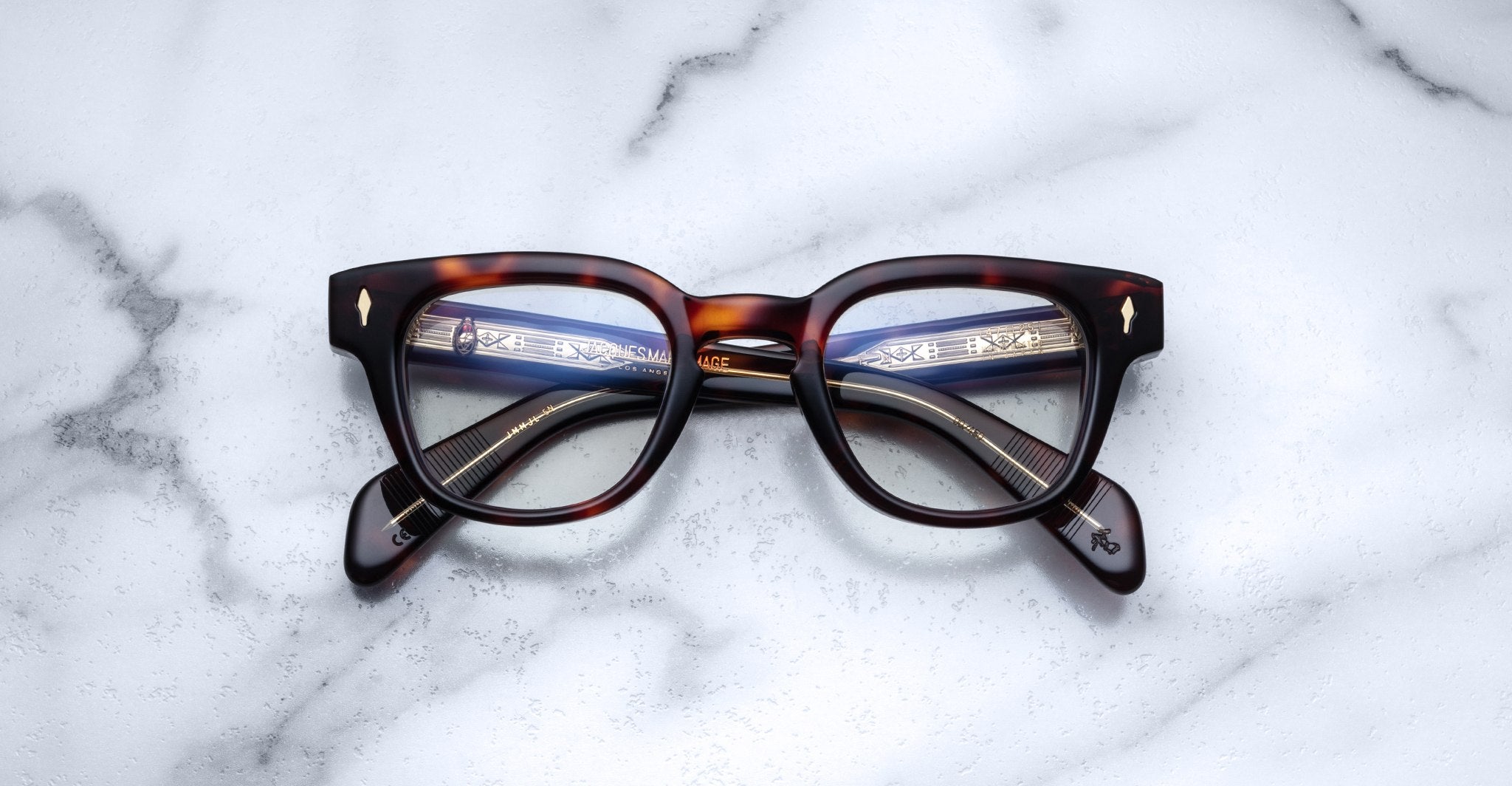 Jacques Marie Mage Julien in Havana 5 rectangular optical frame in rich brown tortoiseshell acetate with subtle amber highlights, featuring a keyhole bridge, signature arrowhead front pins, and exposed metal core detailing within the temples, shown with clear lenses.