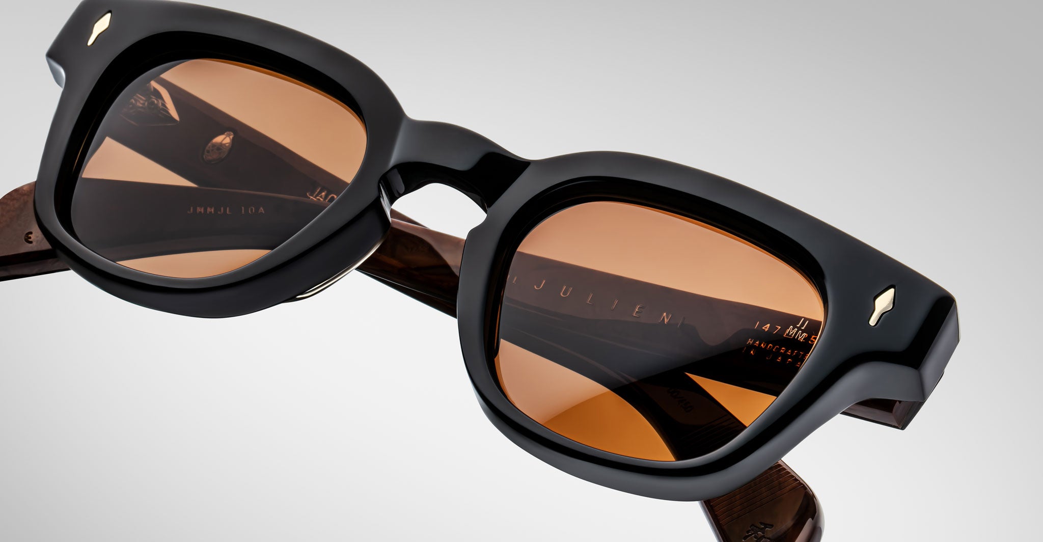 A close-up of Jacques Marie Mage Julien sunglasses, featuring black rectangular frames, brown-tinted lenses, thick temples with small metallic accents, and the brand name visible on the inner arm.