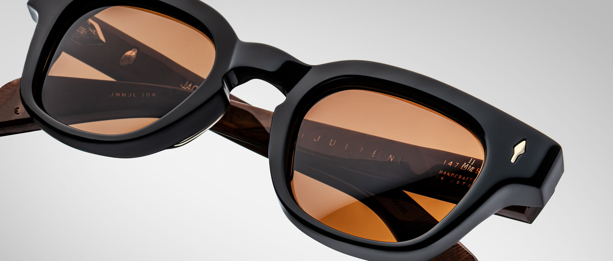 A close-up of Jacques Marie Mage Julien sunglasses, featuring black rectangular frames, brown-tinted lenses, thick temples with small metallic accents, and the brand name visible on the inner arm.