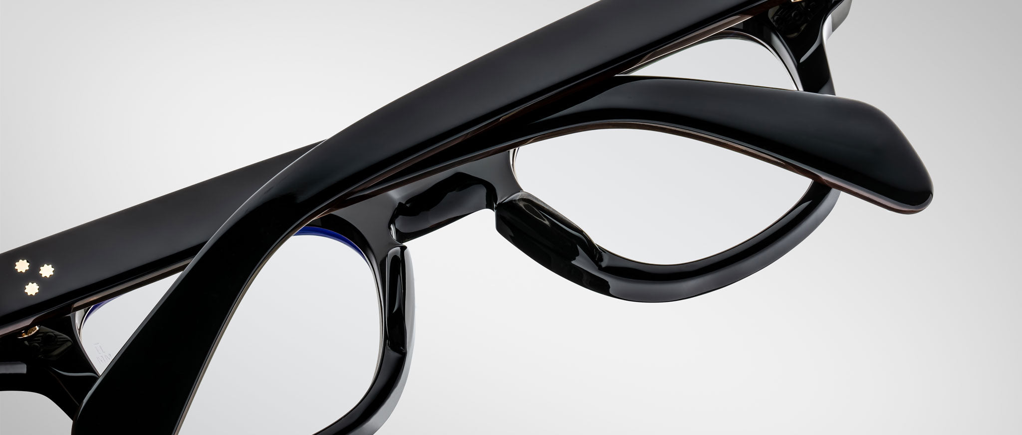Close-up of Jacques Marie Mage Julien black eyeglasses with thick frames and temples, arms crossed over each other, set against a plain light gray background.