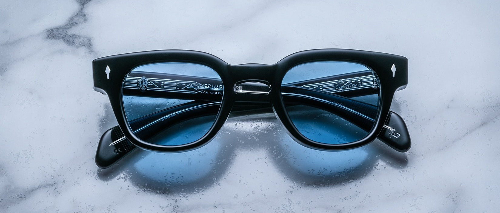 Jacques Marie Mage Julien in Titan rectangular frame in black acetate with cool blue undertones, featuring a keyhole bridge, signature arrowhead front pins, and exposed metal core detailing within the temples, fitted with blue-tinted lenses.