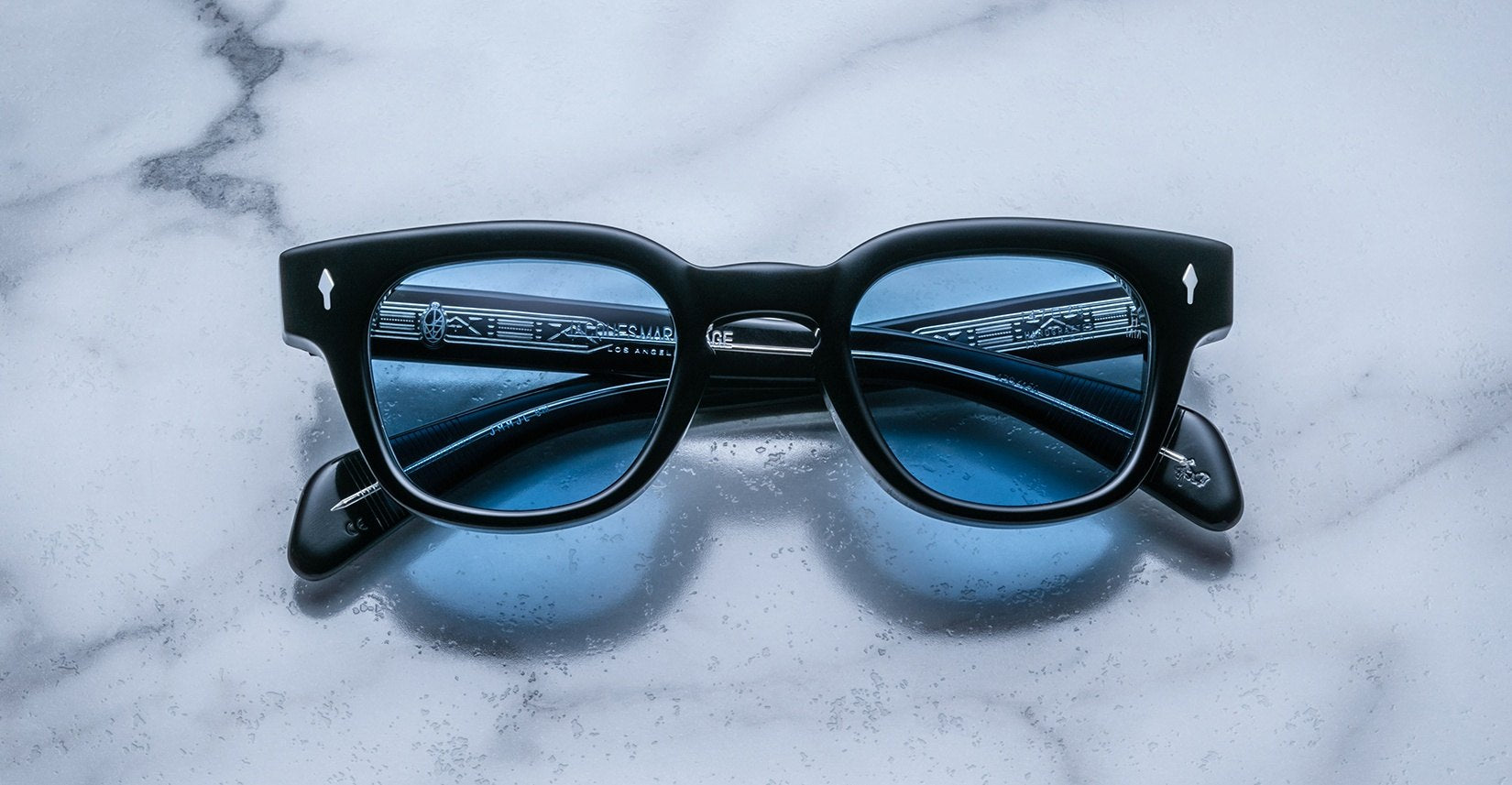 Jacques Marie Mage Julien in Titan rectangular frame in black acetate with cool blue undertones, featuring a keyhole bridge, signature arrowhead front pins, and exposed metal core detailing within the temples, fitted with blue-tinted lenses.