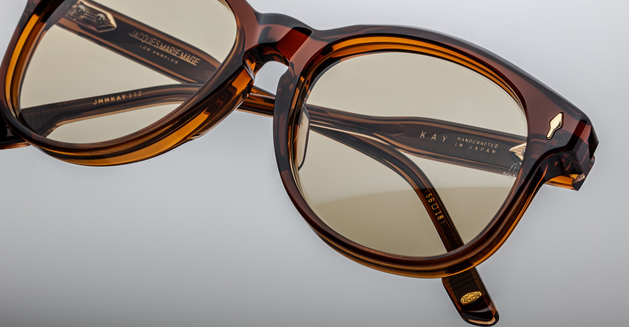 Close-up of Jacques Marie Mage Kay sunglasses in Teak brown with yellow-tinted lenses, highlighting fine craftsmanship and engraved inner arms, set against a neutral background.