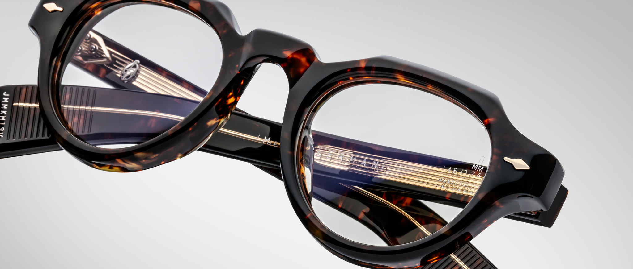 Close-up of Jacques Marie Mage Kellerman eyeglasses featuring round lenses and gold-detailed arms, displayed at an angle on a neutral background. Both the frame’s tortoiseshell design and lens details are clearly visible.