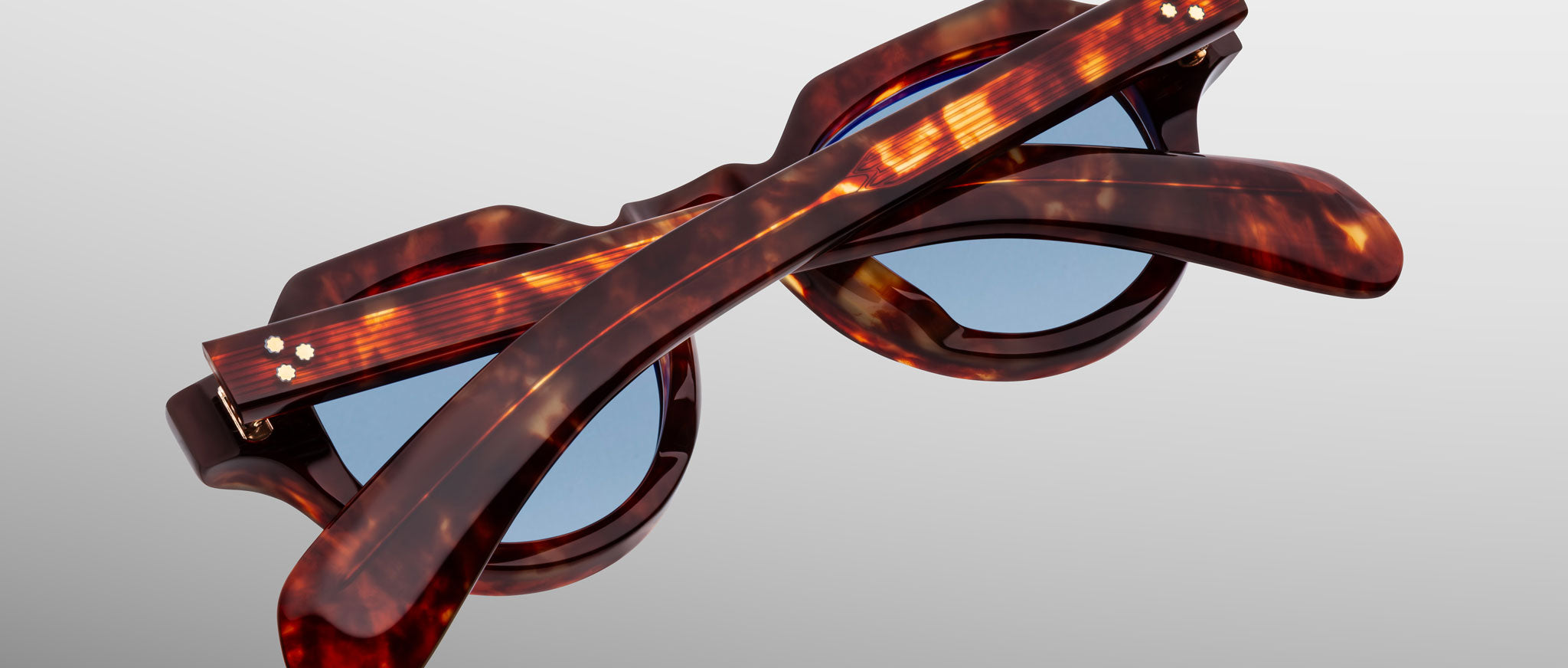 The Jacques Marie Mage Kellerman sunglasses, featuring tortoiseshell frames and blue lenses, are shown folded shut on a light gray background in a top-down view that highlights their elegant design.