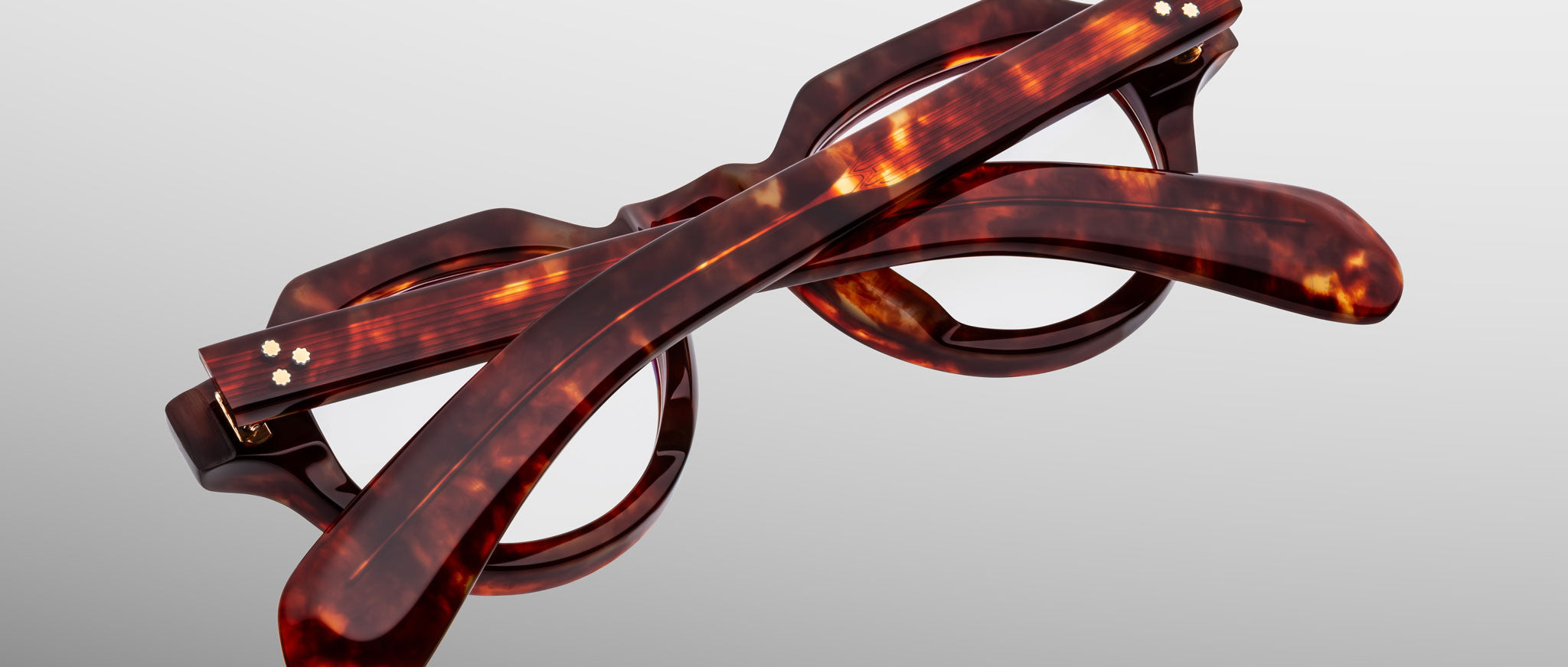 A pair of Jacques Marie Mage Kellerman tortoiseshell round-frame eyeglasses is folded and photographed against a neutral gray background.