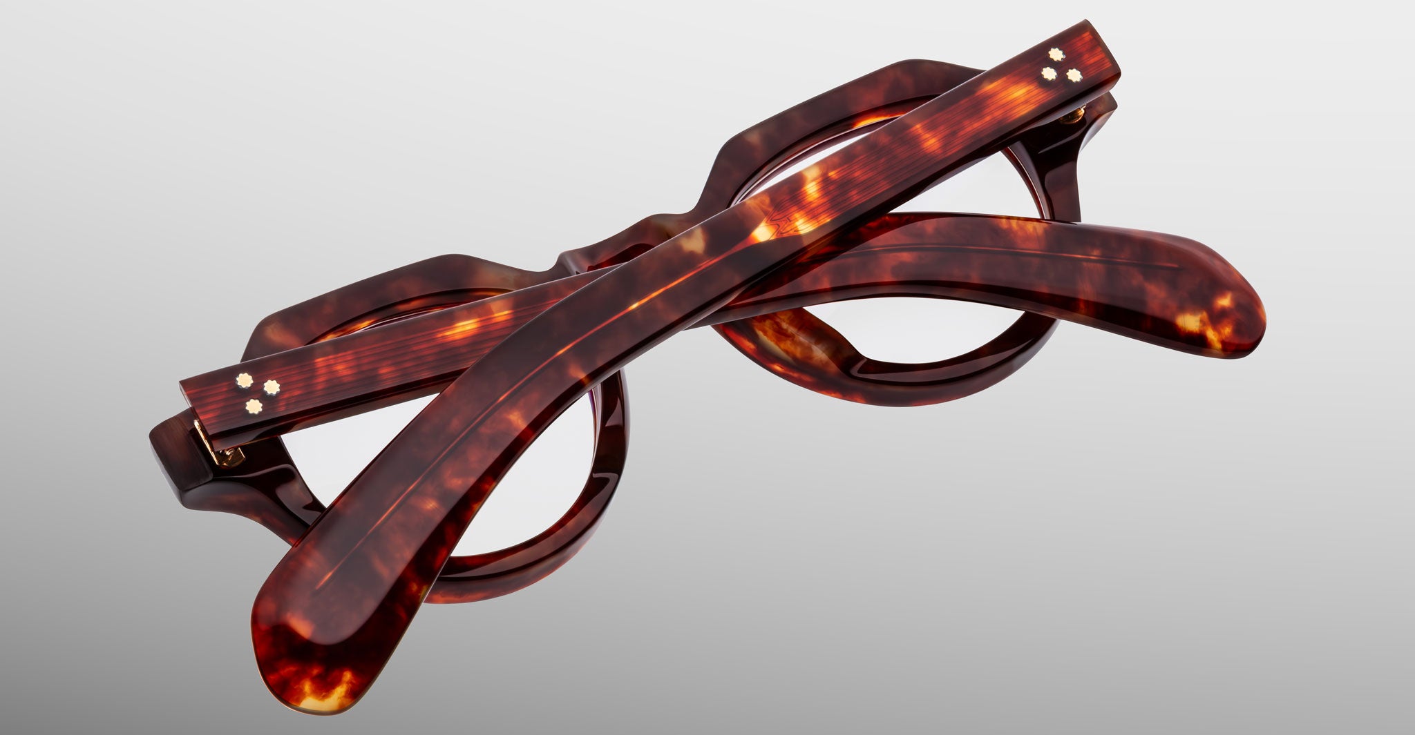 A pair of Jacques Marie Mage Kellerman tortoiseshell round-frame eyeglasses is folded and photographed against a neutral gray background.