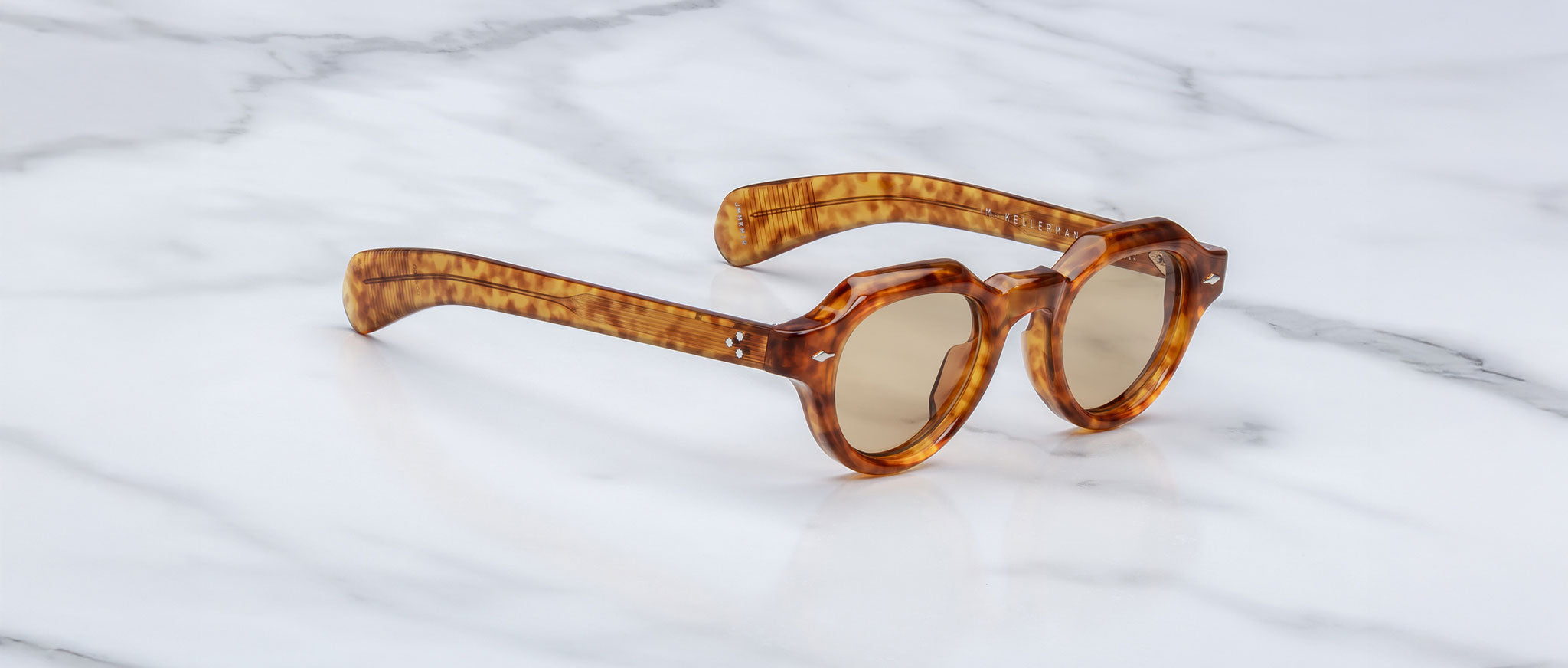 The Jacques Marie Mage Kellerman sunglasses, featuring a tortoiseshell pattern and round lenses, rest on a white marble surface.