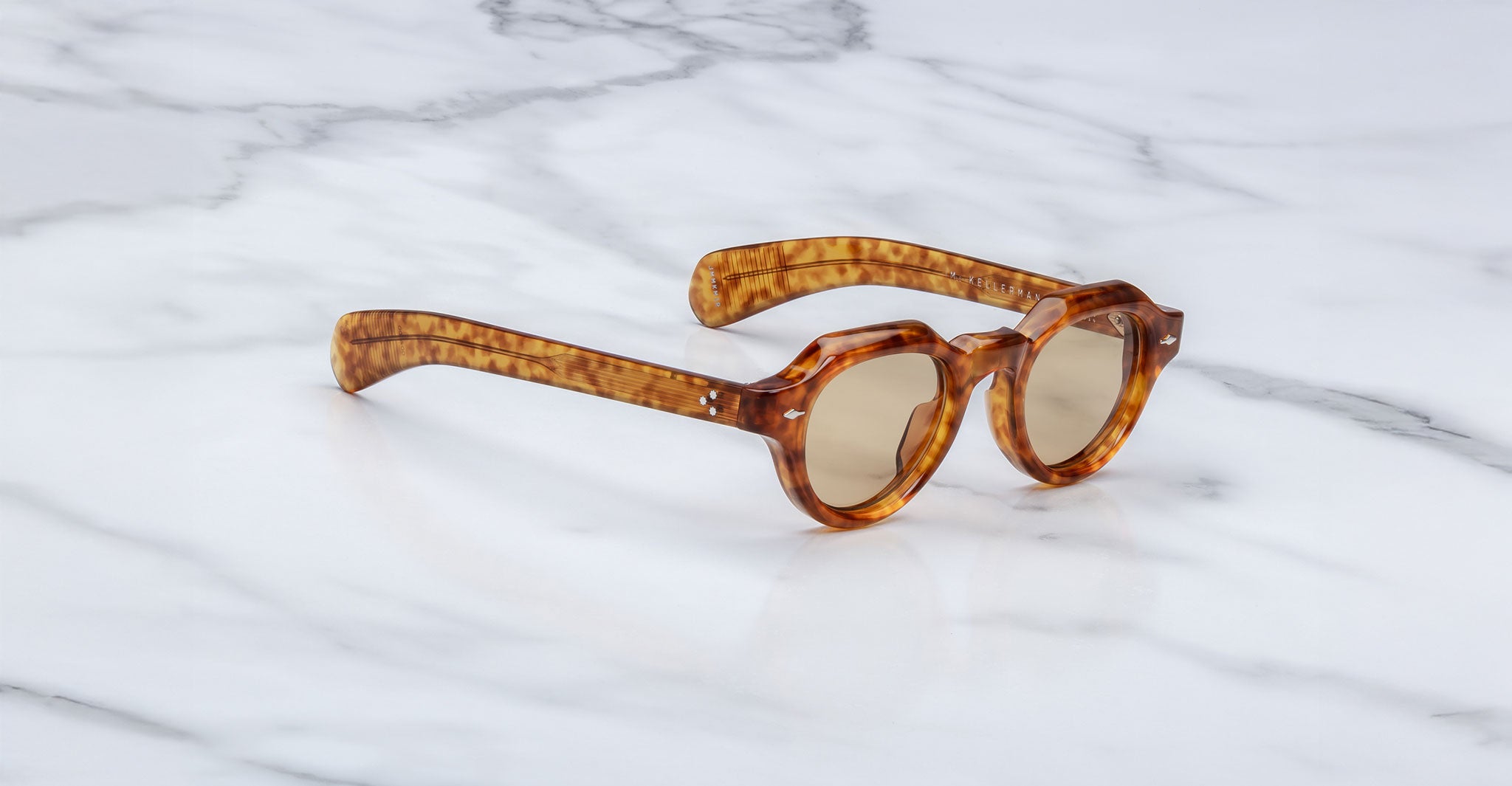 The Jacques Marie Mage Kellerman sunglasses, featuring a tortoiseshell pattern and round lenses, rest on a white marble surface.