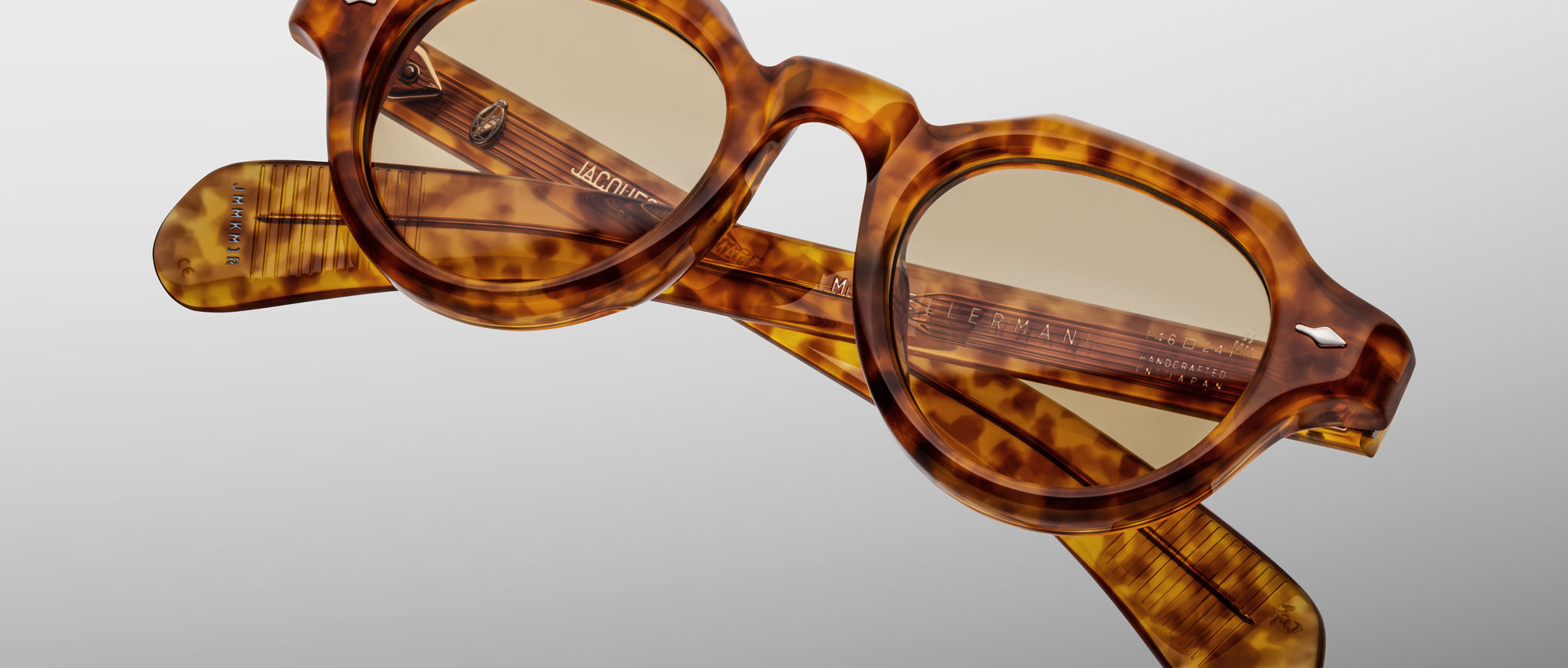 The Jacques Marie Mage Kellerman, round tortoiseshell eyeglasses with thick frames and lightly tinted lenses, are displayed diagonally with folded arms against a plain gray background.