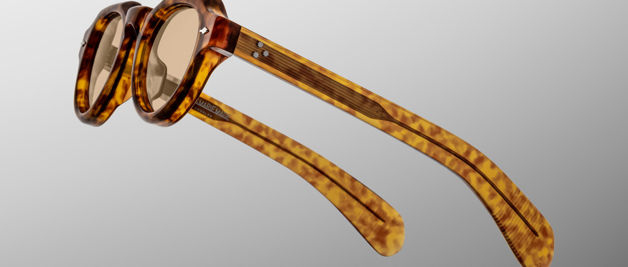 The Jacques Marie Mage Kellerman eyeglasses feature round lenses and thick tortoiseshell frames with patterned arms, displayed from a side angle against a plain gray background.