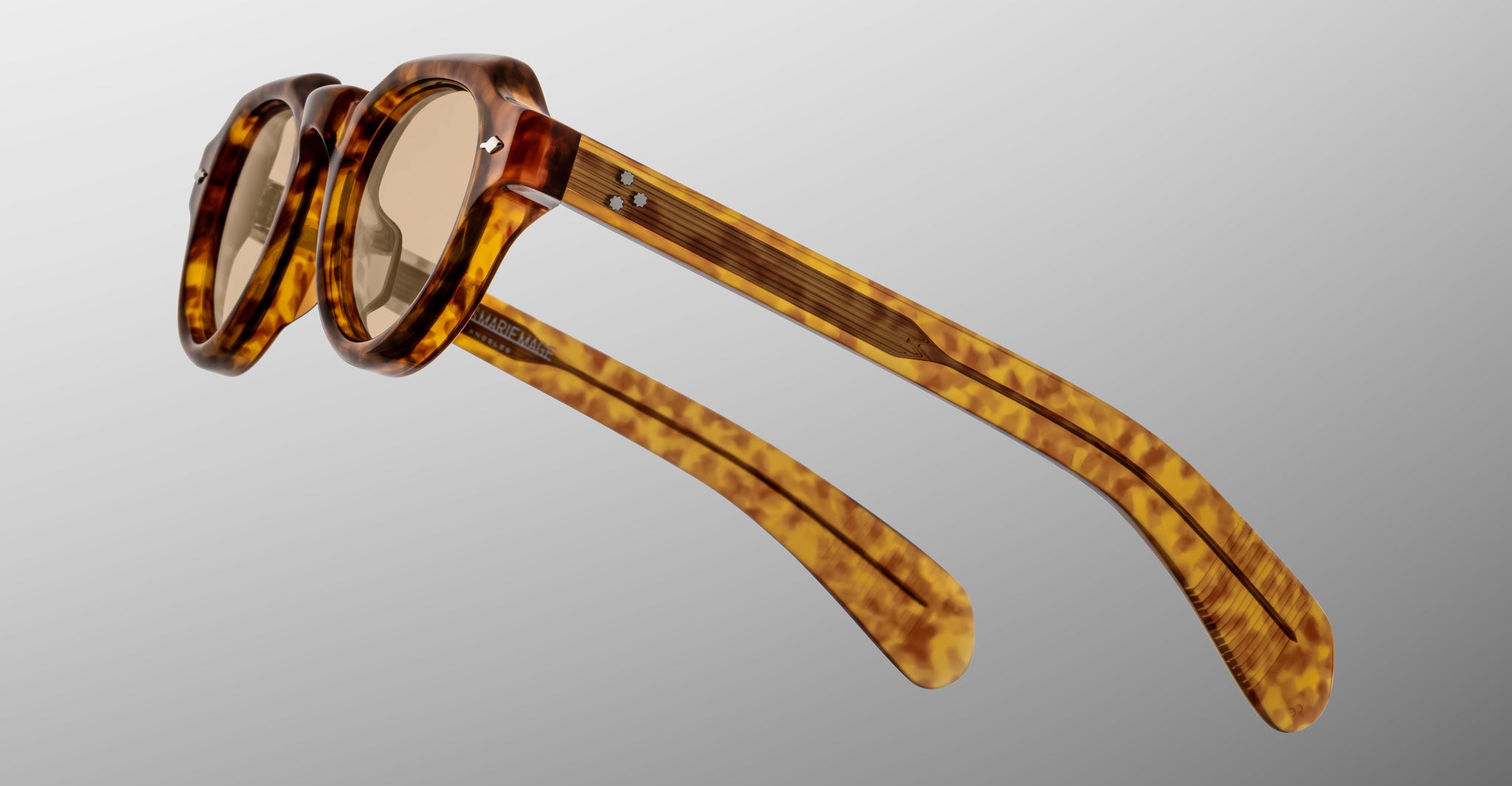 The Jacques Marie Mage Kellerman eyeglasses feature round lenses and thick tortoiseshell frames with patterned arms, displayed from a side angle against a plain gray background.