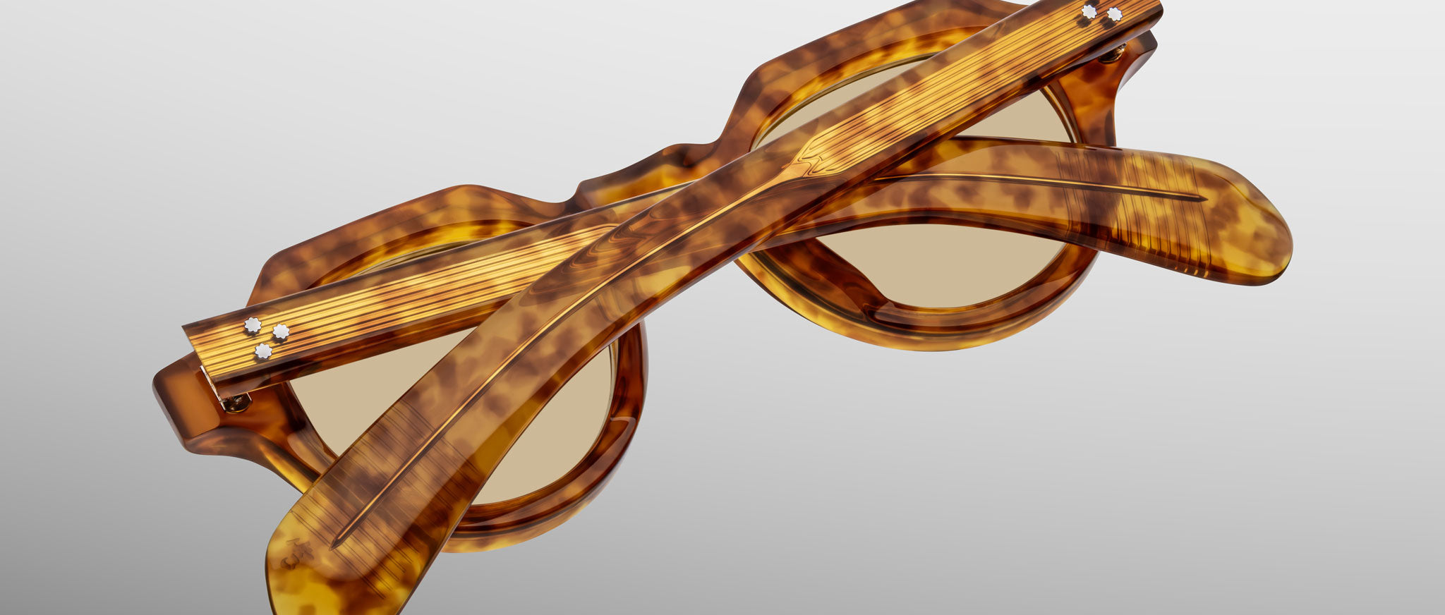 A pair of Jacques Marie Mage Kellerman sunglasses in a tortoiseshell pattern is displayed folded, with the arms crossed over the lenses, set against a soft gradient background.