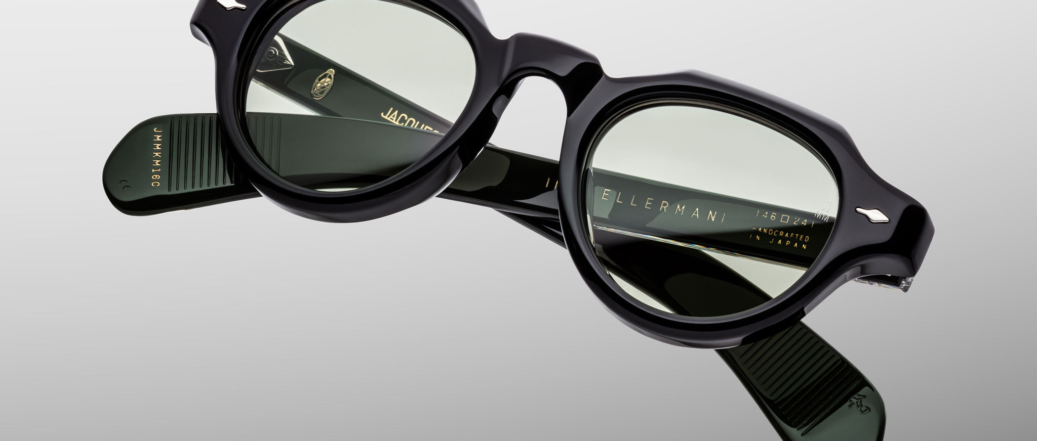 The Jacques Marie Mage Kellerman features black round eyeglasses with slightly tinted lenses, displayed on a light grey background. The temples showcase brand markings and gold lettering details.