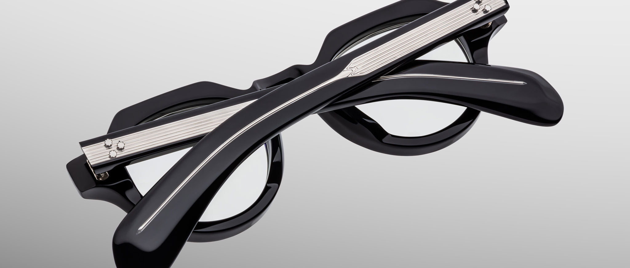 The Jacques Marie Mage Kellerman eyeglasses, featuring black round frames with silver accents, are shown folded with crossed temples on a plain gray background.
