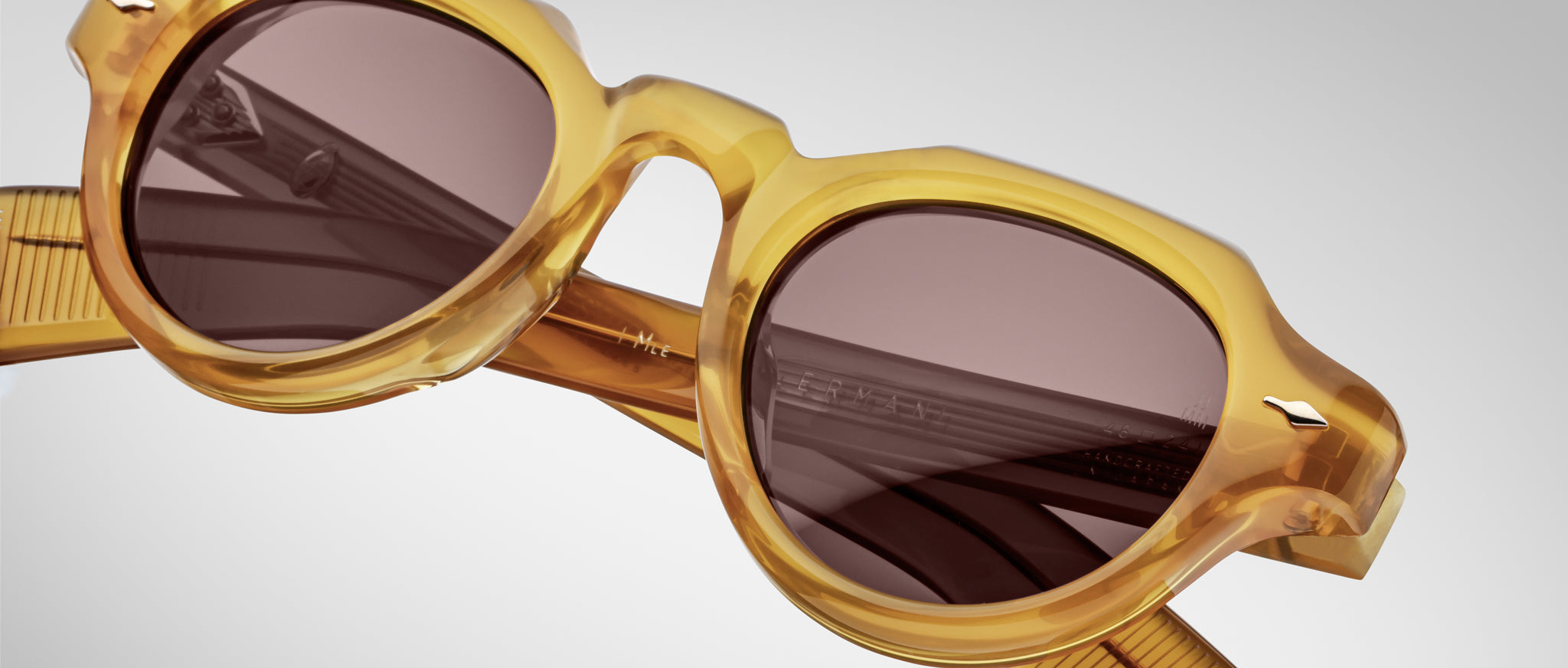 Close-up of Jacques Marie Mage Kellerman sunglasses featuring thick, translucent yellow frames and dark round lenses. The light, blurred background accentuates the eyewear’s texture and stylish details.