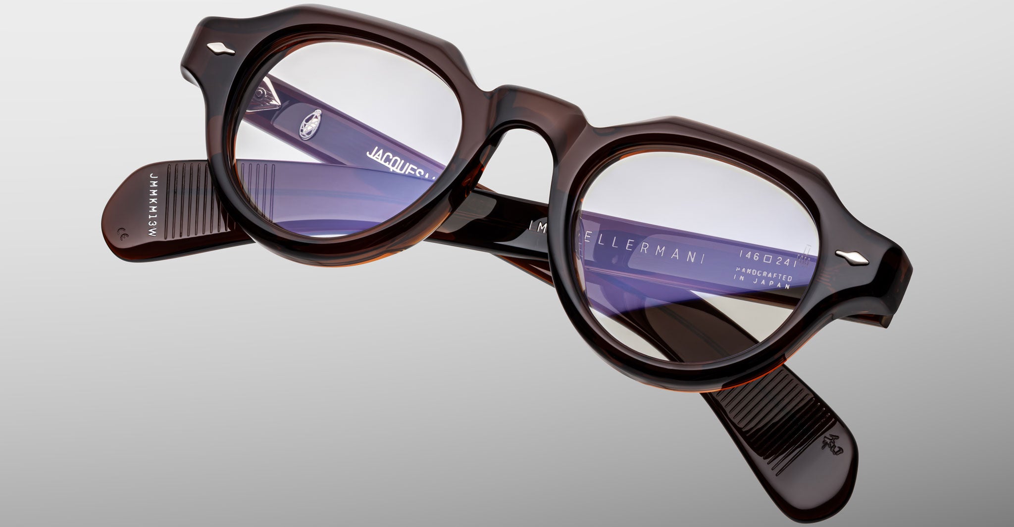 The Jacques Marie Mage Kellerman eyeglasses feature round, dark tortoiseshell thick frames with clear lenses, displayed on a light gray background. Branding and product details appear in white text on the inner arms.