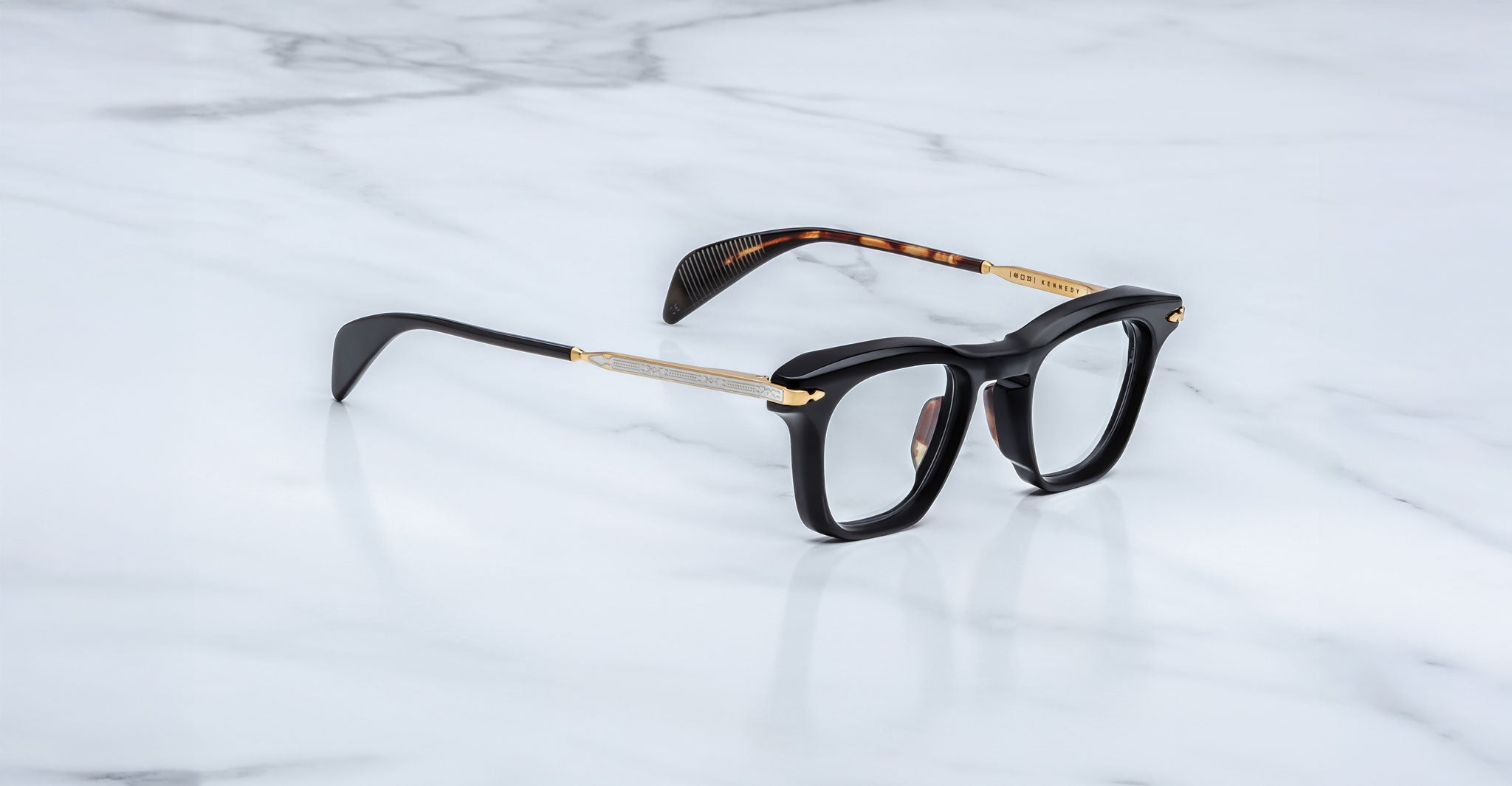 Jacques Marie Mage Kennedy rectangular eyeglasses in black and gold, tortoiseshell temples, front view.