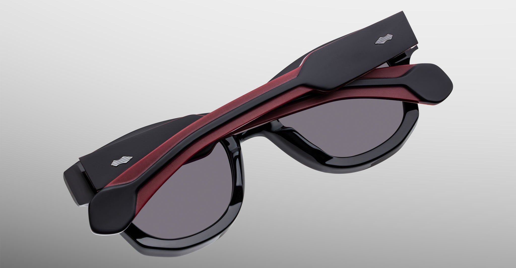 Jacques Marie Mage Kinshasa sunglasses, folded, black frame, dark lenses, red accent, silver logo on the arms, side view.