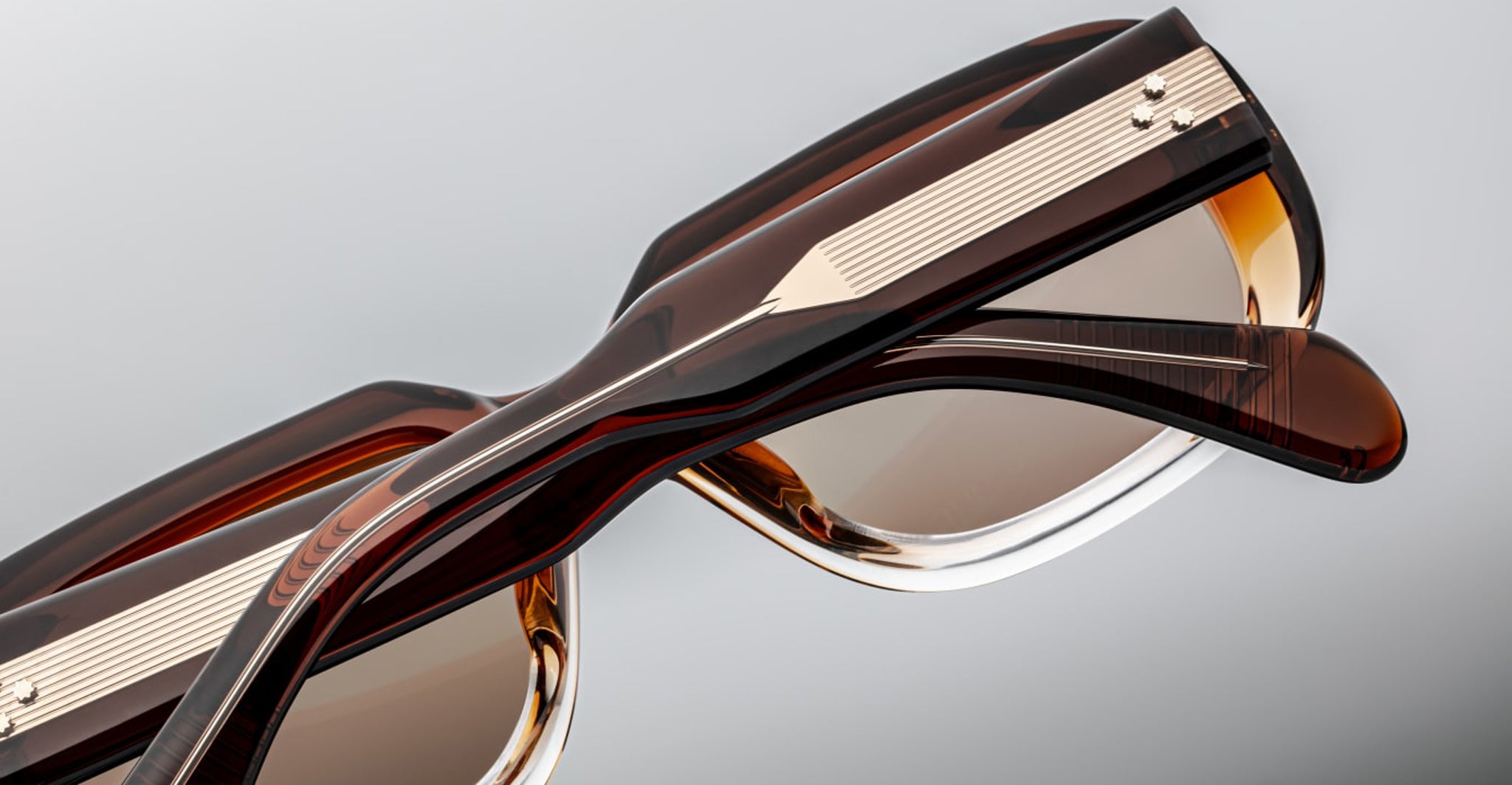 Close-up of two pairs of Jacques Marie Mage Kobo sunglasses with gold accents, stacked front view.