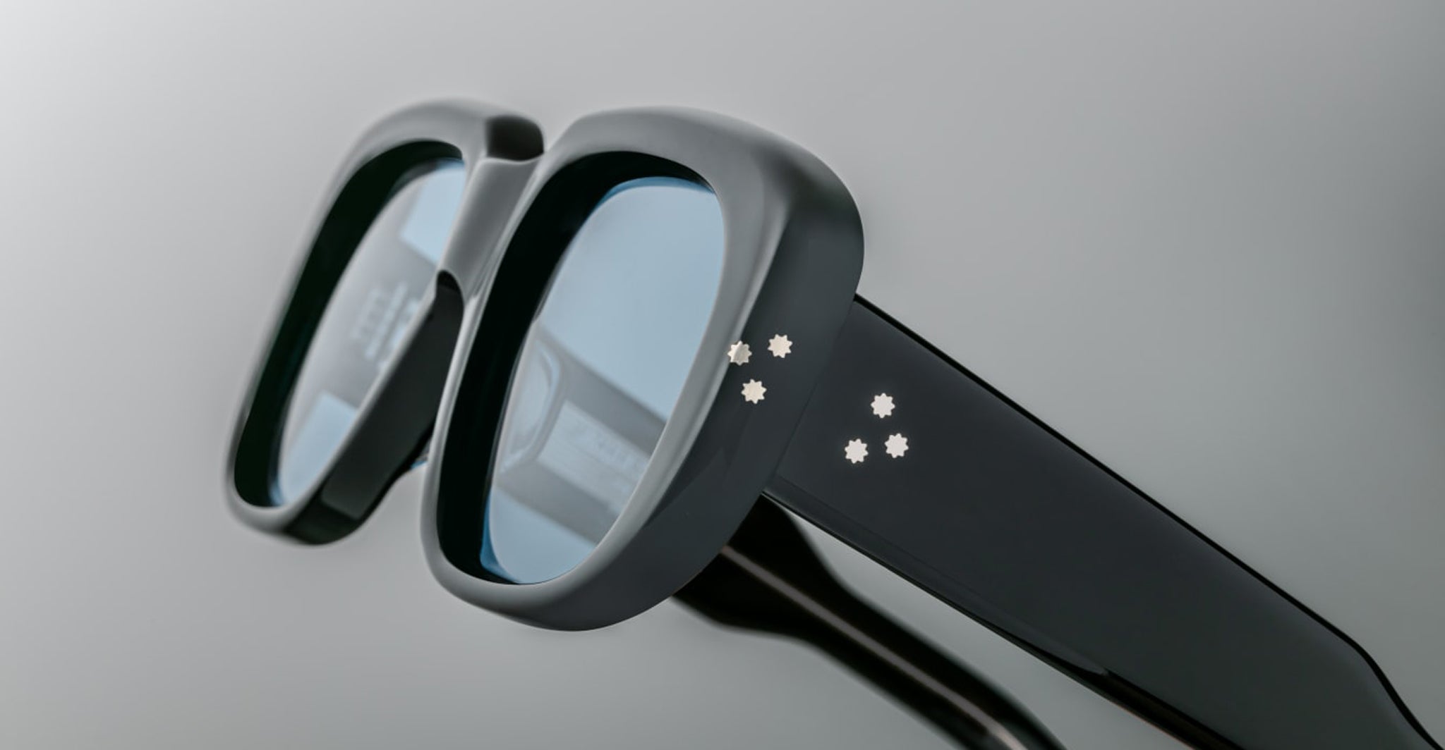 Close-up of Jacques Marie Mage Kobo eyeglasses with blue-tinted lenses and star-shaped accents on a black frame.