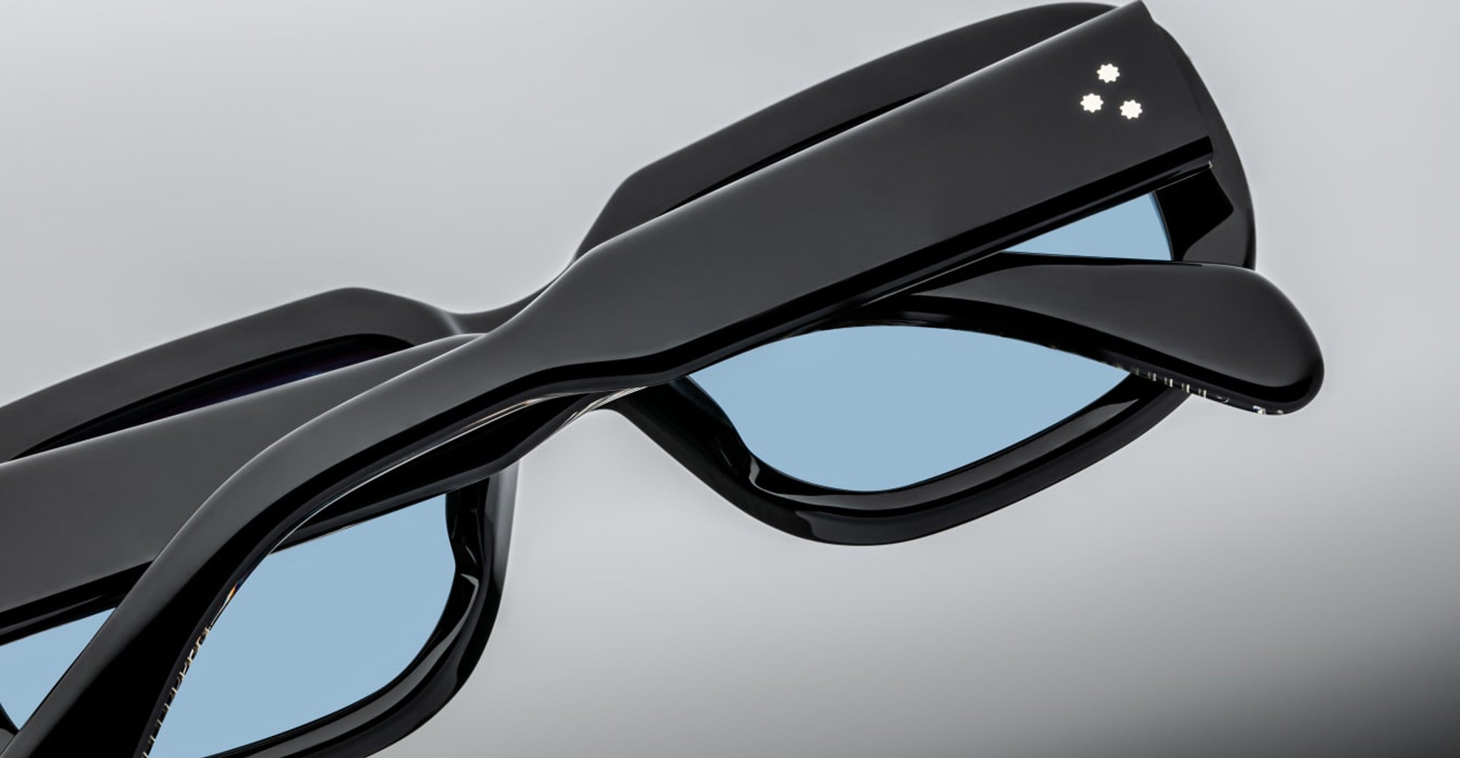 Close-up of two Jacques Marie Mage Kobo black smart eyeglasses with blue-tinted lenses and three white dots on the frames.