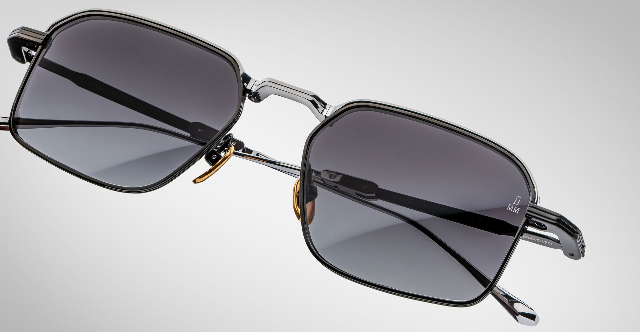A close-up of Jacques Marie Mage Koenig sunglasses featuring modern rectangular dark lenses, thin metal frames, and adjustable nose pads, set on a plain light gray background.