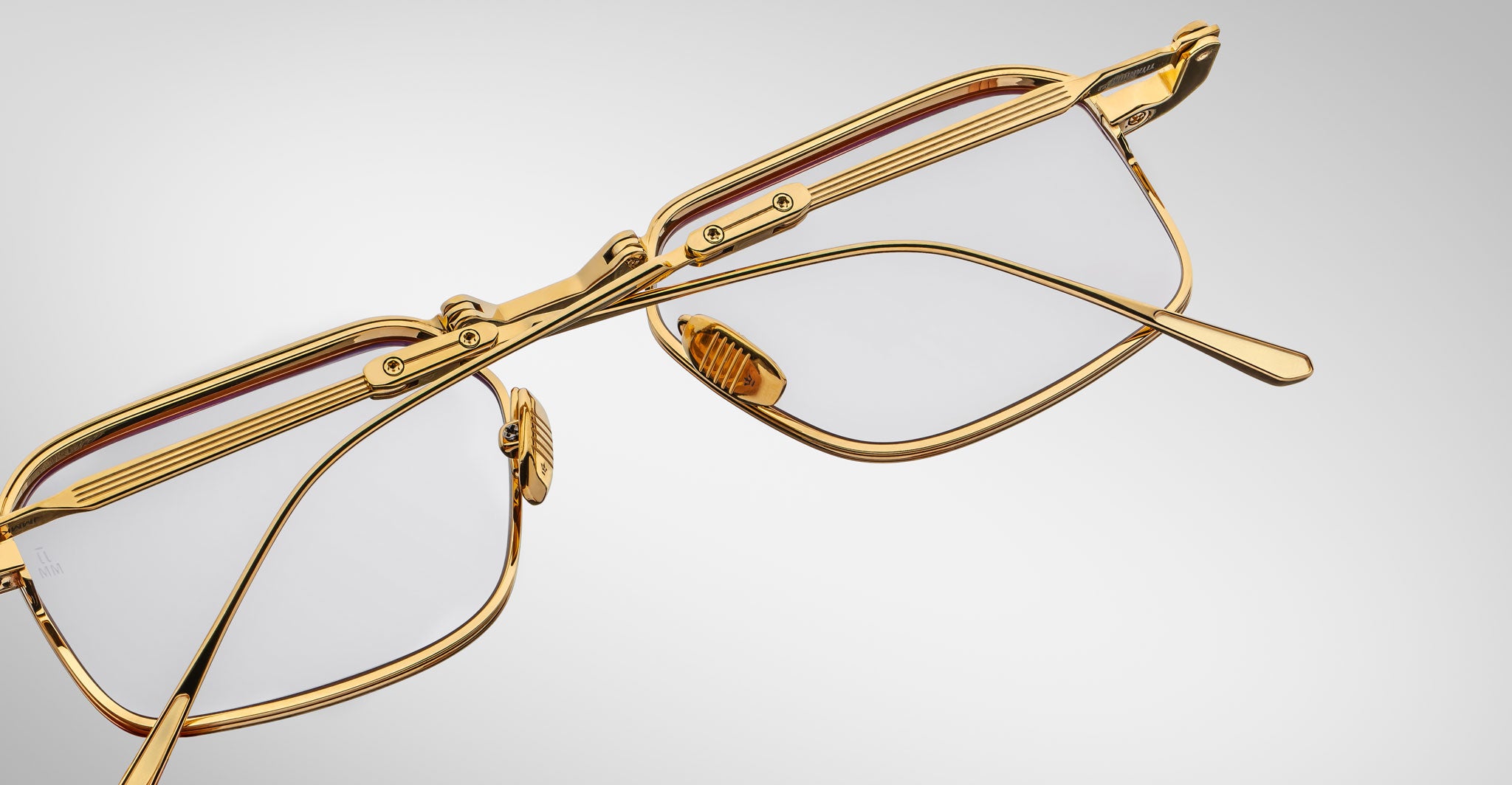A close-up of Jacques Marie Mage Koenig gold-framed eyeglasses with clear lenses, set against a white background and angled to showcase the temple hinges and detailed design.