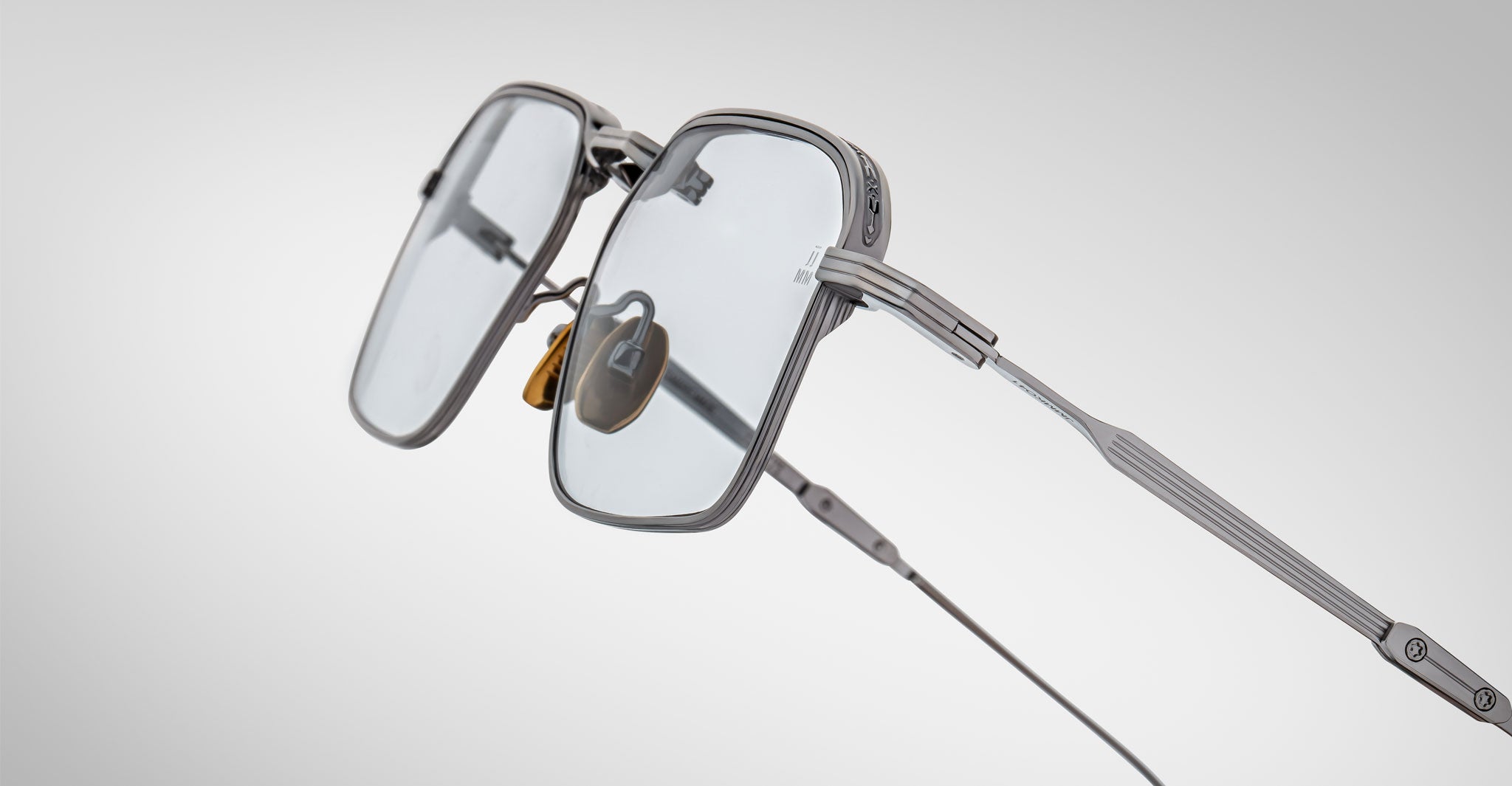 Close-up of Jacques Marie Mage Koenig eyeglasses featuring modern, square-shaped thin metallic frames and clear lenses against a gradient background, highlighting the frame design and nose pads.