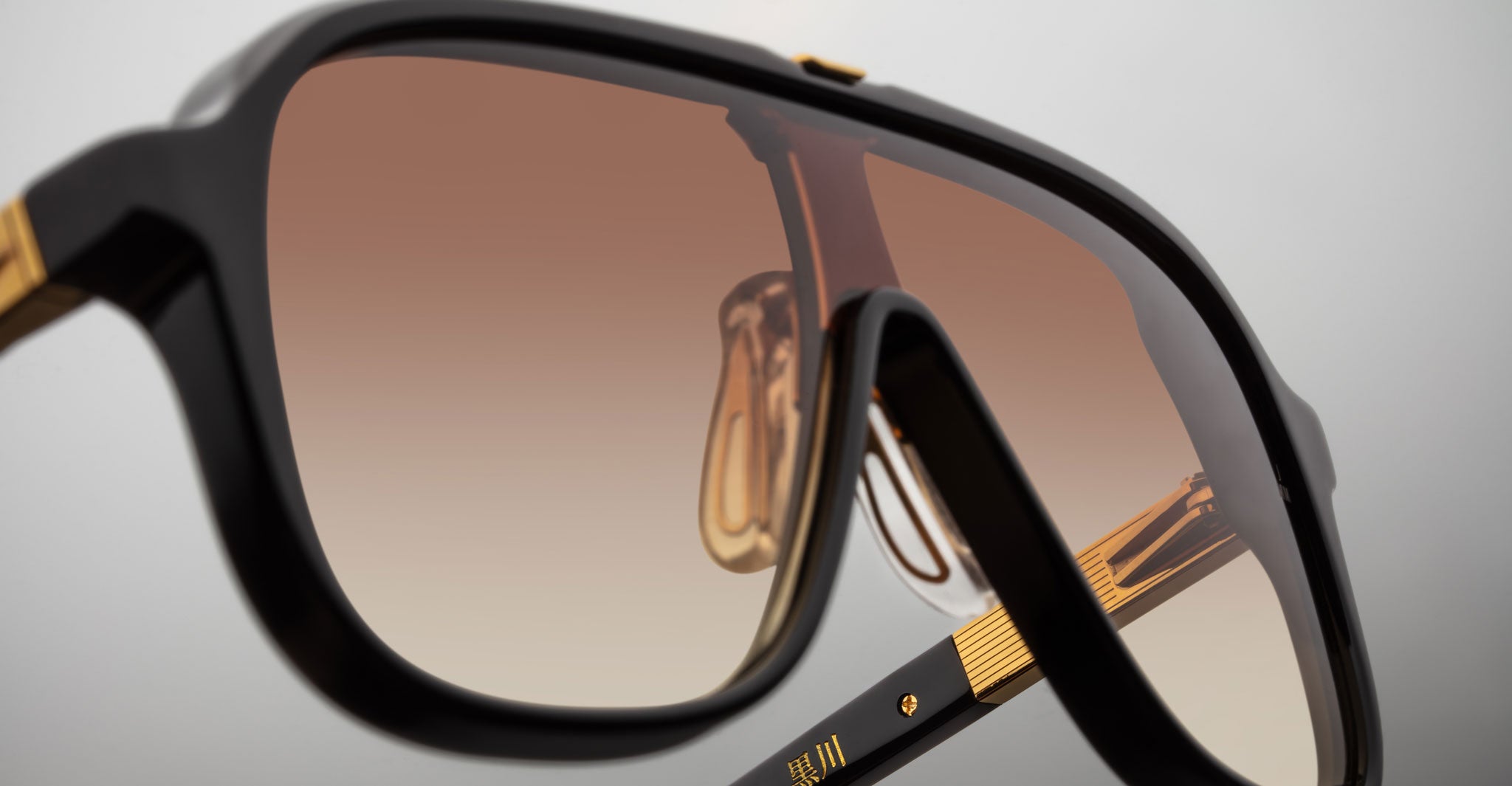 Close-up of Jacques Marie Mage Kurokawa sunglasses featuring dark frames, gold accents, and brown gradient lenses, highlighting the detailed texture and reflective surface.